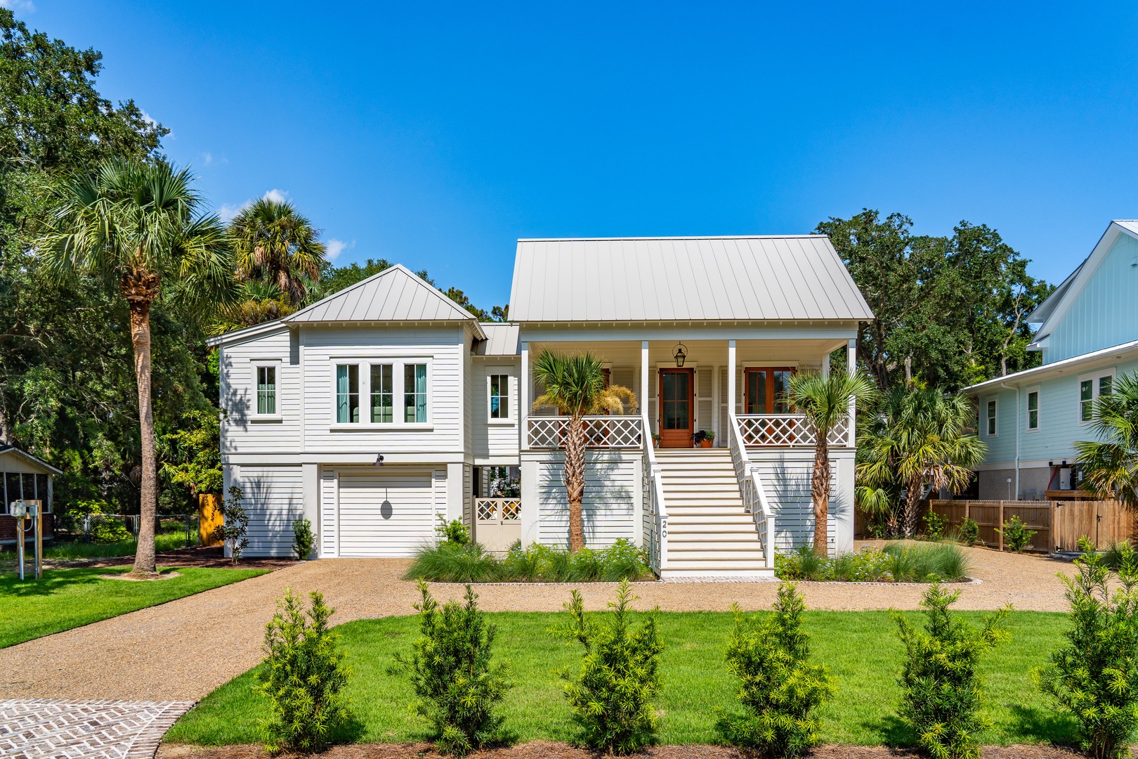 This charming coastal cottage features a welcoming covered porch framed by palm trees and lush landscaping, set in a peaceful residential neighborhood with ample parking and beautifully manicured grounds.