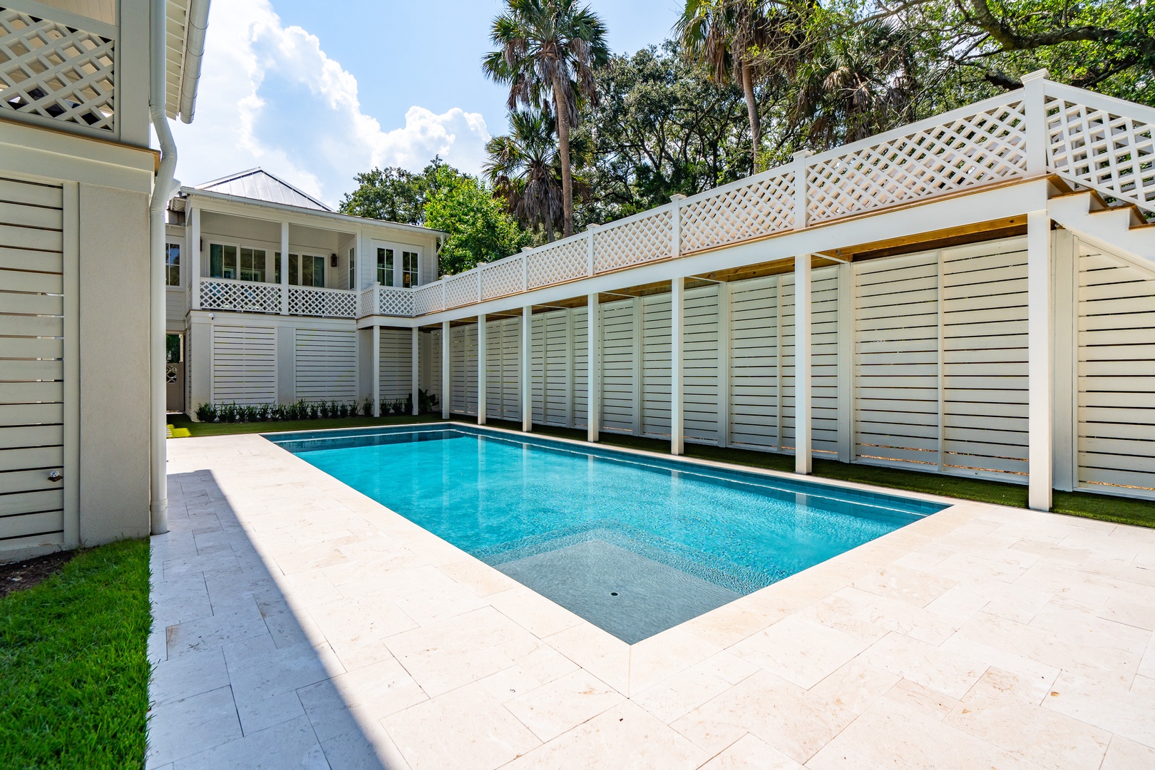 Your private pool retreat is framed by tropical palms and elegant lattice fencing, creating a serene sanctuary under bright Florida skies.