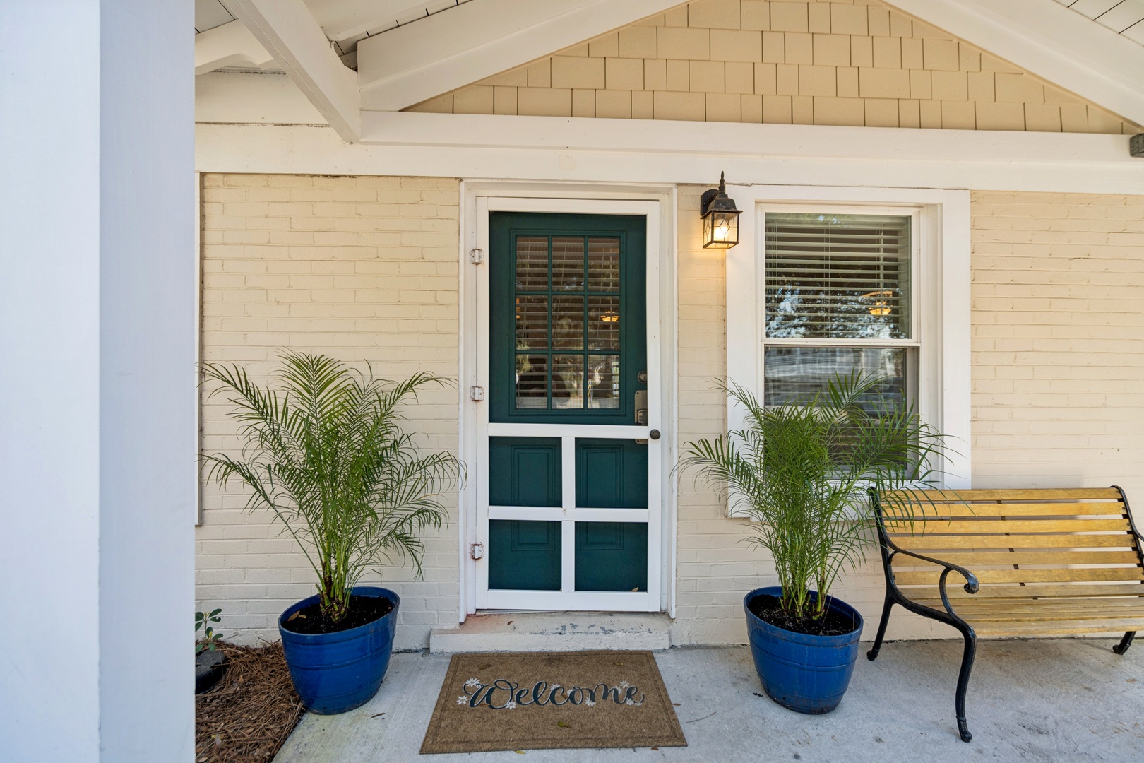 A welcoming entrance with charming teal door, tropical palms, and cozy bench creates the perfect arrival experience for your getaway.