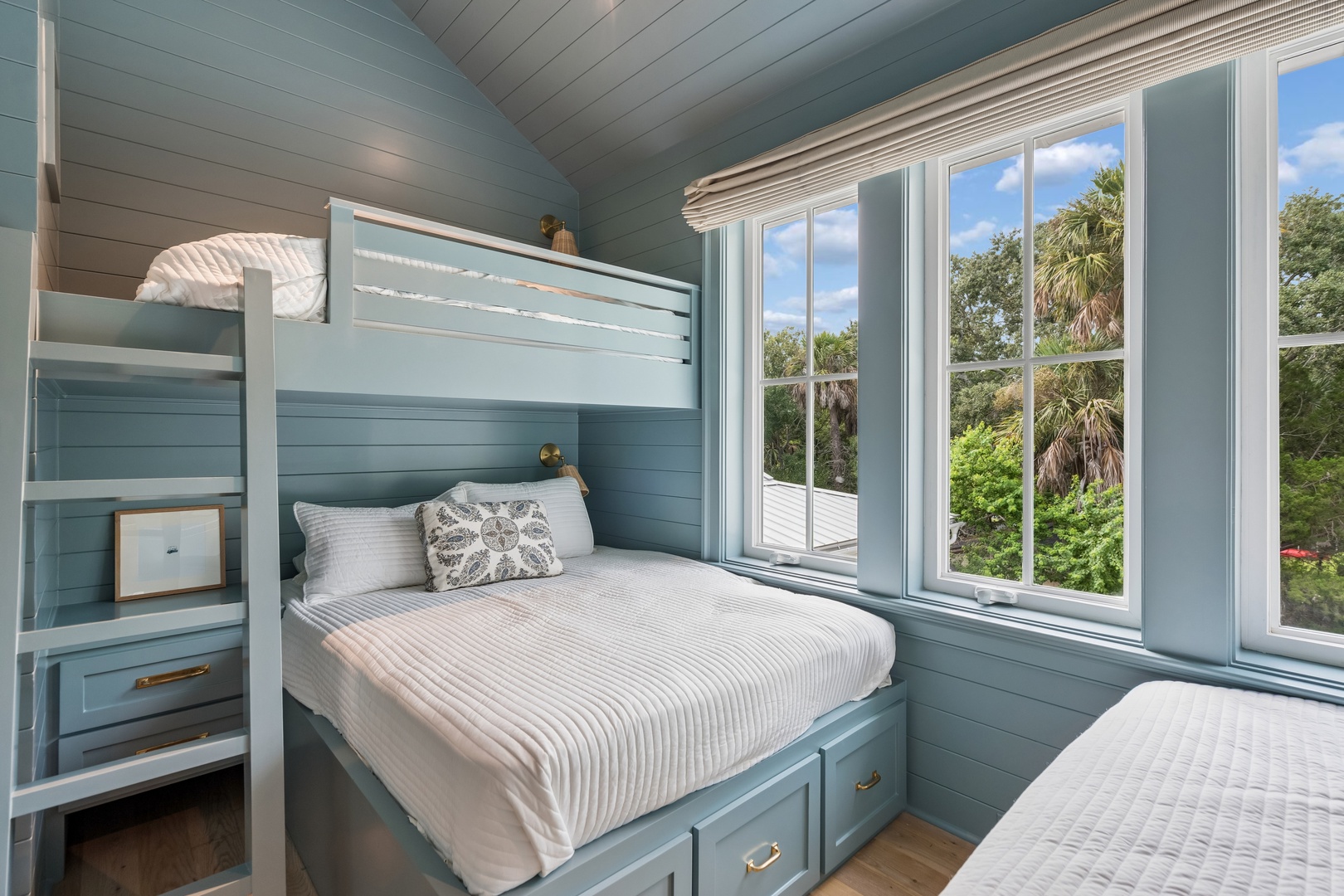 Rest easy in this charming coastal bedroom with custom bunk beds and warm wood floors. Large windows invite natural light while framing views of lush tropical greenery.