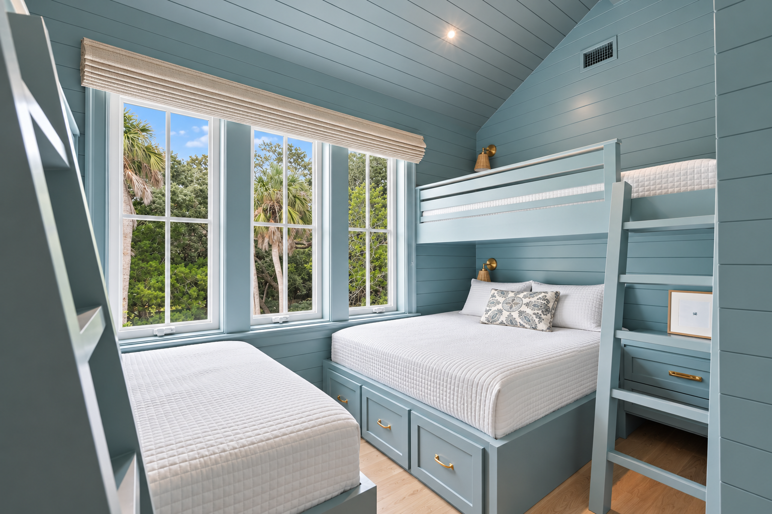 Your coastal retreat features custom bunk beds with crisp linens and under-bed storage, framed by cheerful windows overlooking lush palm trees and greenery.