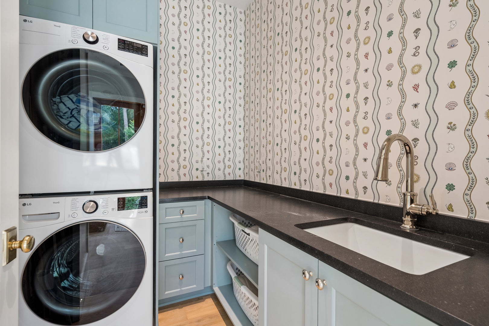 A cheerful laundry space with modern stacked washer and dryer, charming ocean-themed wallpaper, and a sleek countertop with sink—making your laundry routine feel anything but ordinary.