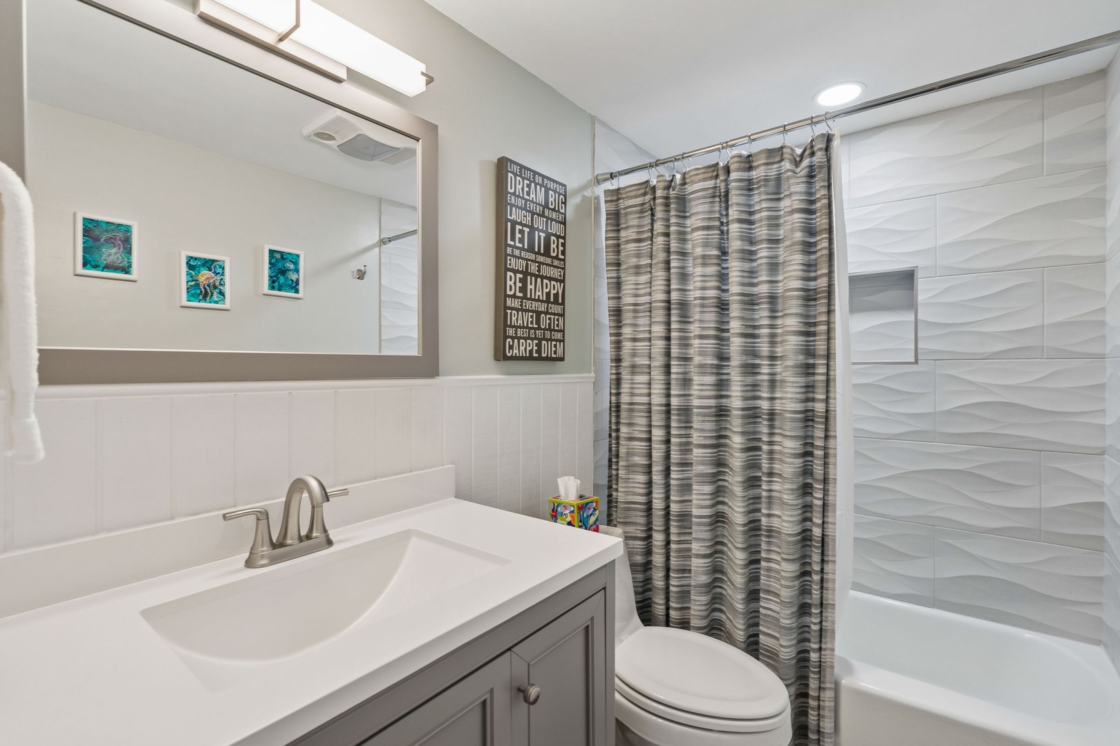 Refresh in your modern bathroom featuring elegant wave-textured tiles, inspiring artwork, and thoughtful amenities including kid-friendly touches.