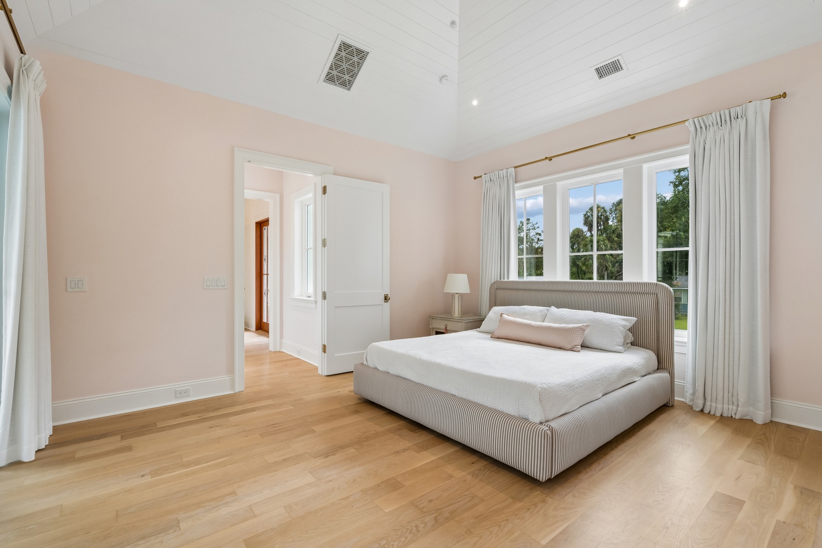 Wake up to a fresh, tranquil retreat with high ceilings and warm natural light. Your comfortable bed invites restful sleep, while large windows frame peaceful garden views.