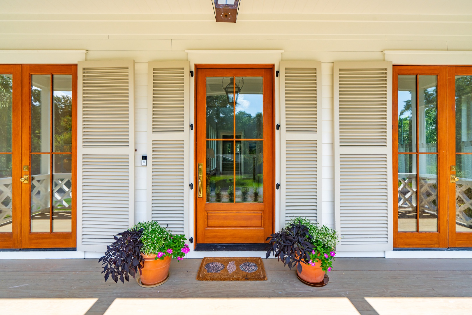 The property's elegant front entrance features classic shuttered windows and a welcoming wood-framed door with decorative planters, set against a pristine white facade.