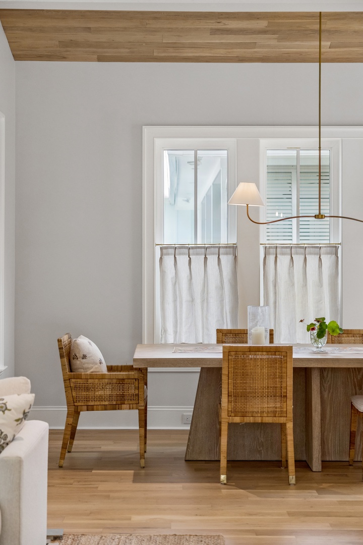 Picture yourself enjoying meals at this elegant dining table, where natural light streams through sheer café curtains and warm wood tones create an inviting coastal atmosphere.