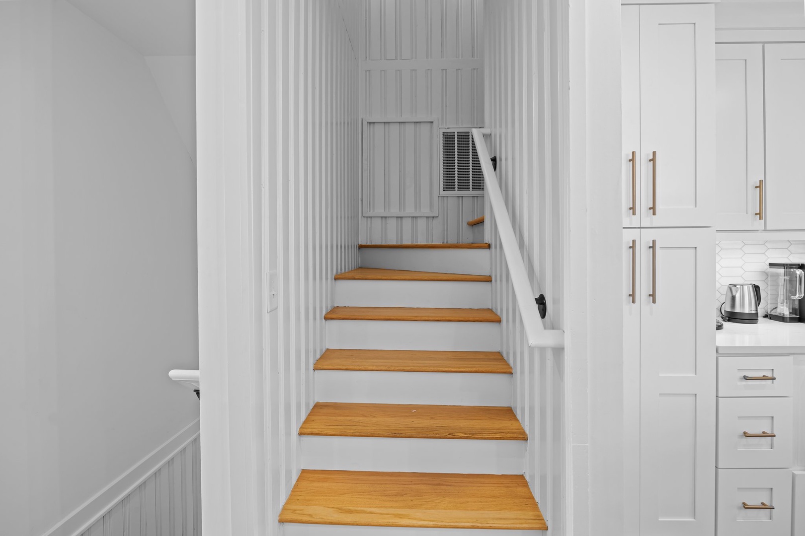 Ascend these beautiful wooden steps to your upstairs retreat, where white shiplap walls and elegant brass fixtures create coastal charm throughout your home.