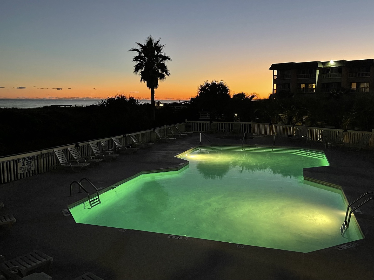 Illuminated pool area surrounded by tropical palms creates a stunning sunset backdrop for the beachfront property.