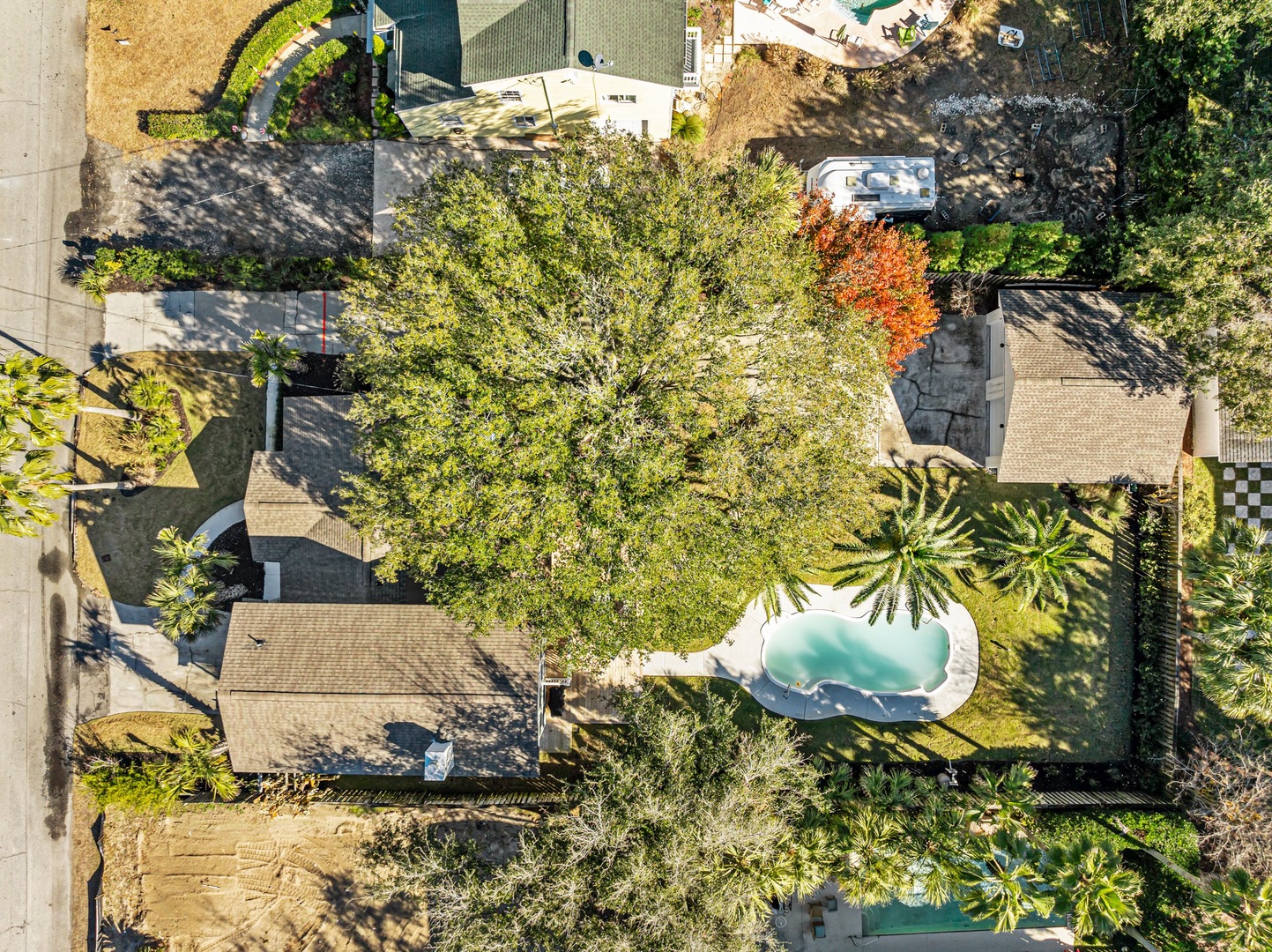 Aerial view showcases the property's spacious grounds with lush tropical landscaping, mature trees, and a stunning pool surrounded by gardens.