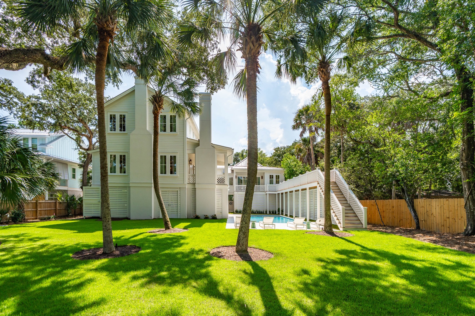 This coastal property features a light green main building with a private pool, surrounded by mature palm trees and landscaped lawn in a serene residential setting.