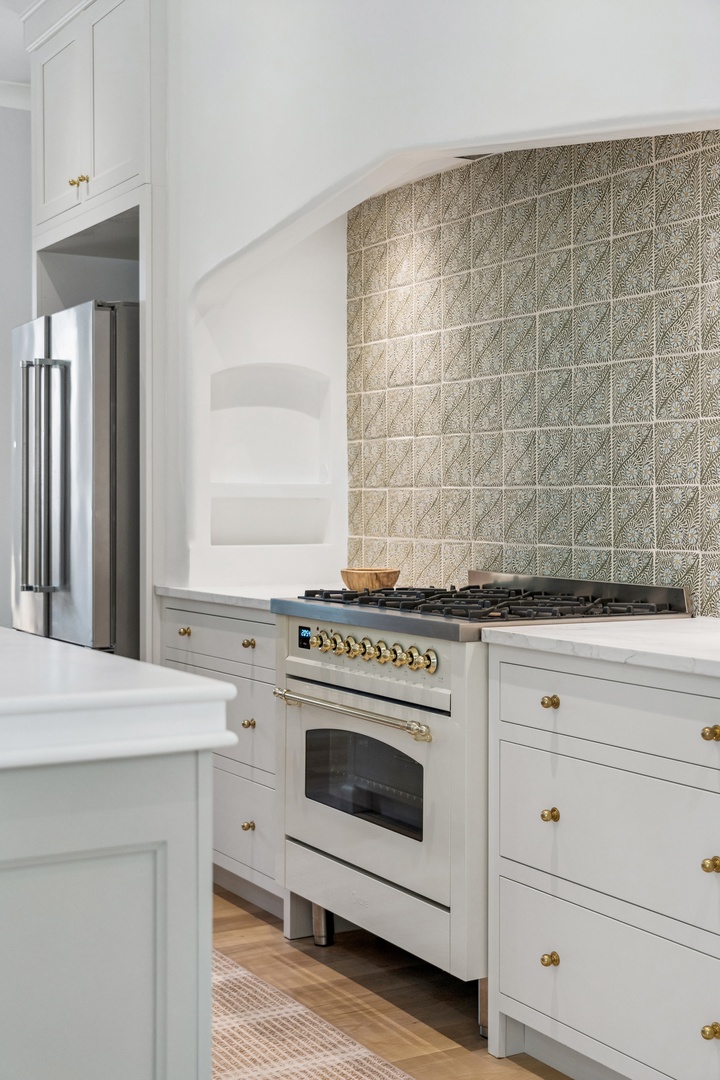 Beautiful kitchen with elegant patterned backsplash, professional-grade gas range, and pristine white cabinetry with brushed gold hardware invites your inner chef.