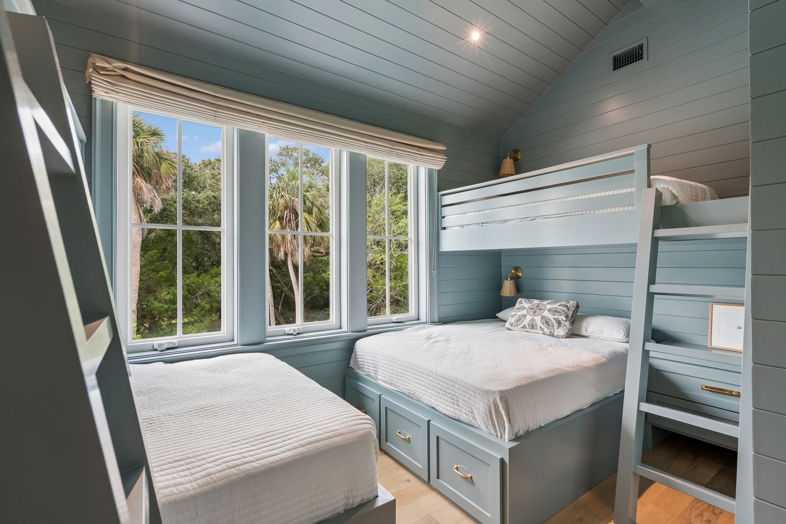 Drift off in this cozy coastal bedroom, where soft bunk beds with built-in storage and calming blue-green walls frame lush tropical views through large windows—your peaceful escape awaits.