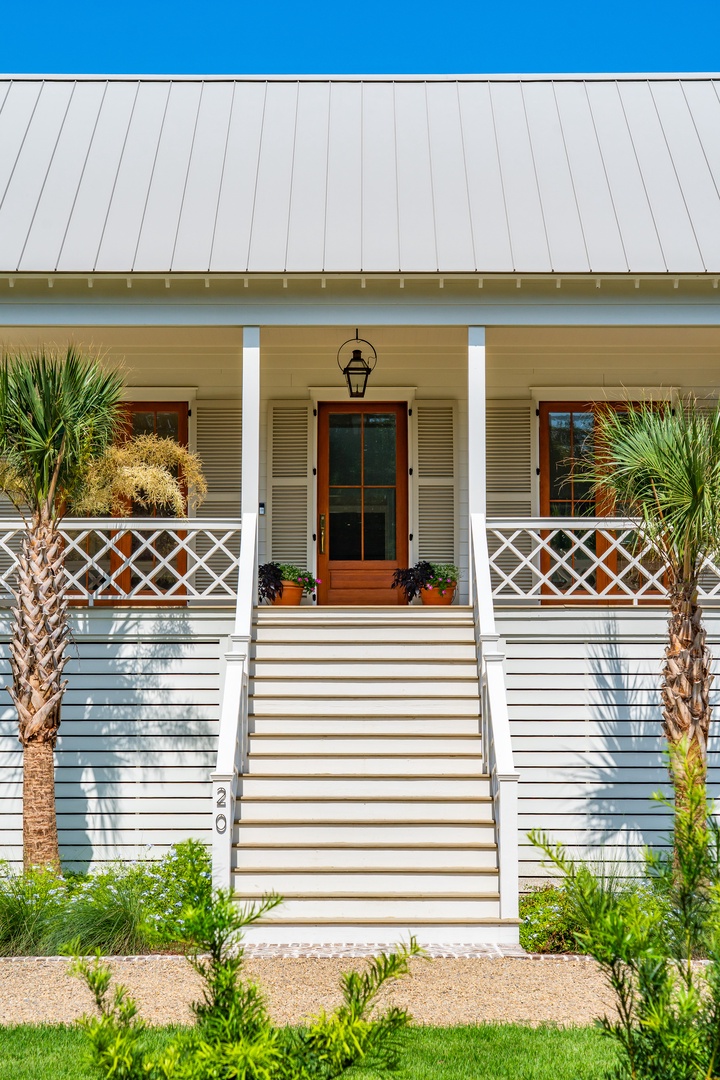 A welcoming coastal-style entrance with charming architectural details, framed by palm trees and a beautifully landscaped pathway leading to the front porch.