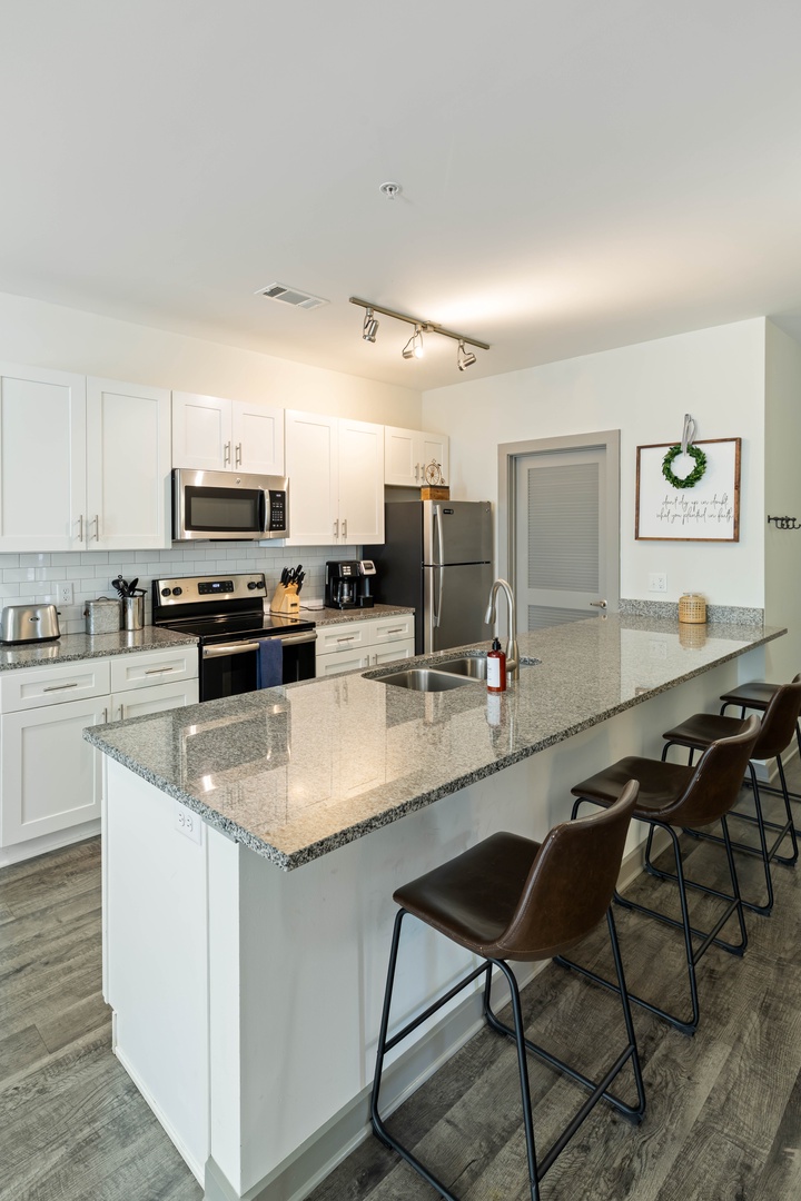 Your fully equipped kitchen awaits, featuring sleek granite countertops, stainless steel appliances, and a spacious island perfect for morning coffee or preparing meals together.