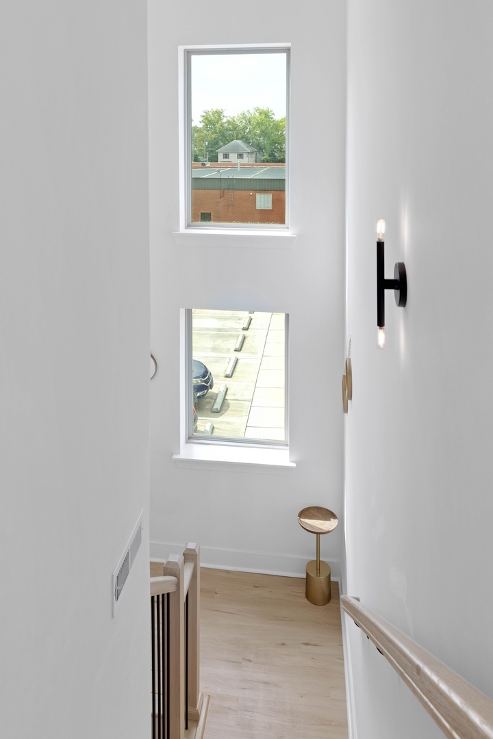 Light pours through tall windows framing your stairwell, where clean white walls and warm wood flooring create a bright, airy path between levels.