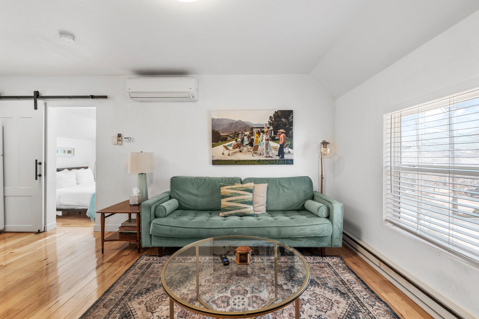 Relax on your plush sage sofa while natural light filters through wooden blinds, creating the perfect atmosphere for afternoon lounging.