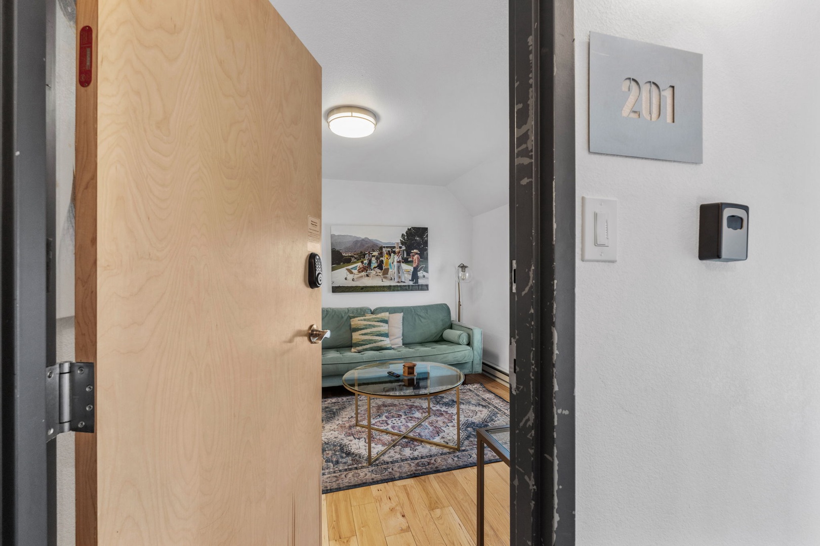 Step into your stylish retreat where modern comfort meets warm wood floors and a plush green sofa perfect for unwinding.