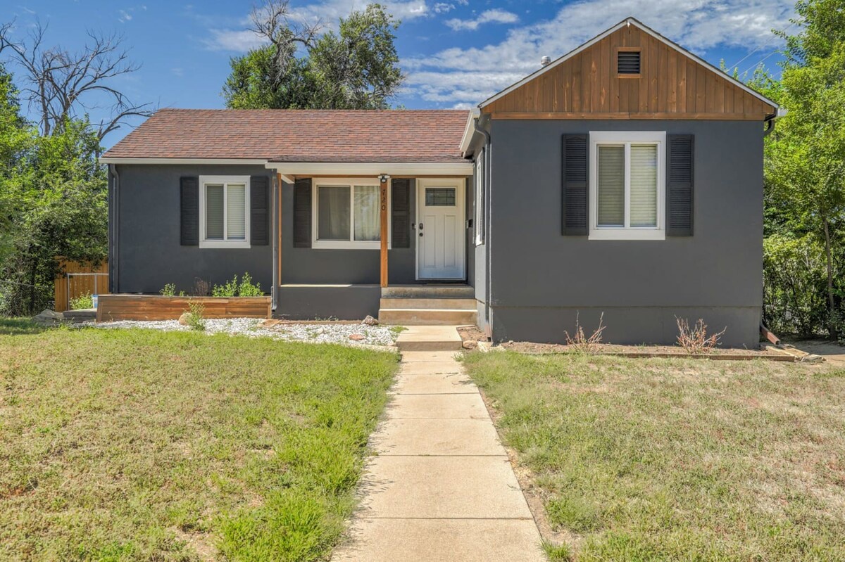 Charming ranch-style home with modern gray exterior and wood accents, nestled among mature trees on a quiet residential street.