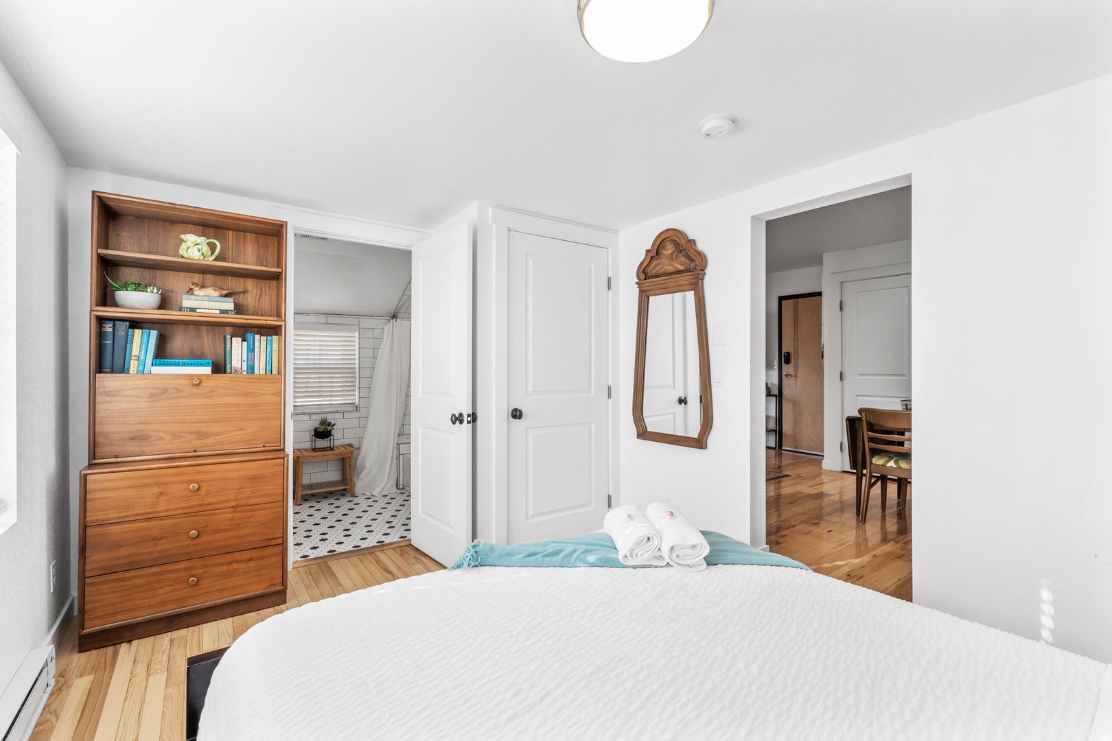 Your comfortable bedroom features a plush bed with crisp white linens, vintage-style mirror, and warm wood furnishings.