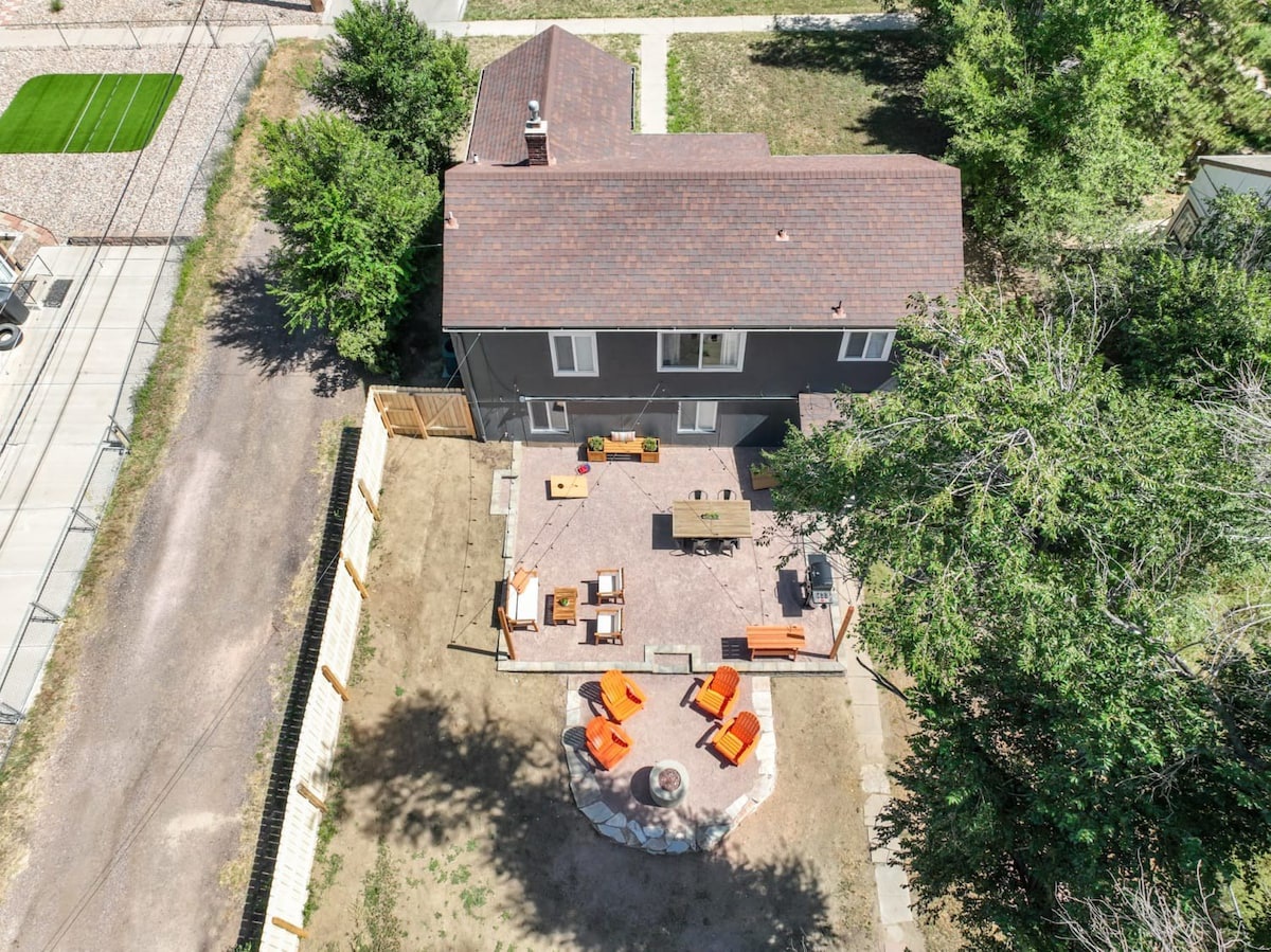 Aerial view of vacation rental property featuring spacious deck, fire pit seating area, and mature trees in quiet neighborhood setting.