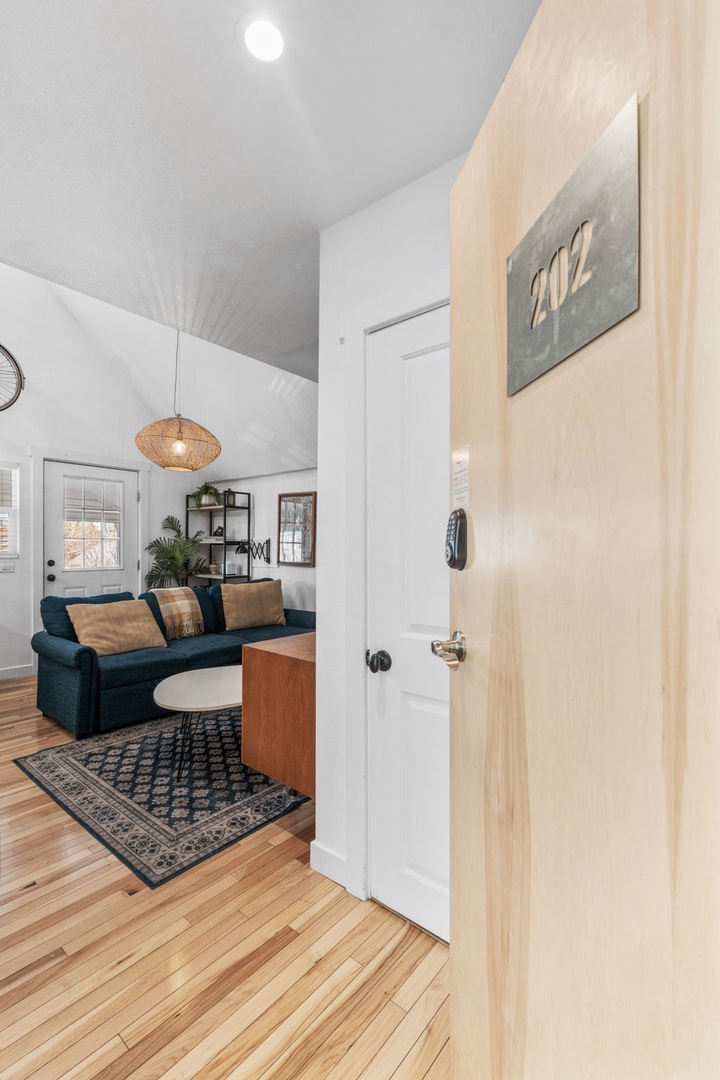 Step into your stylish living space featuring warm hardwood floors, a cozy teal sofa, and thoughtful design touches that make relaxation effortless.