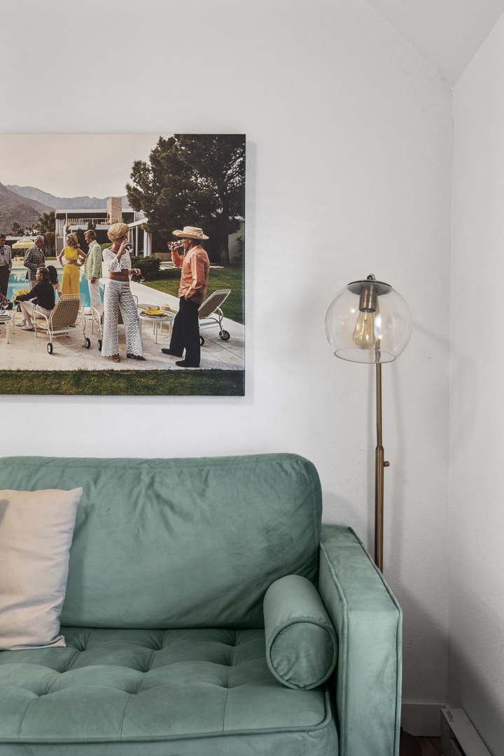 Sink into the plush mint green sofa, where vintage artwork and modern lighting create your perfect reading nook.