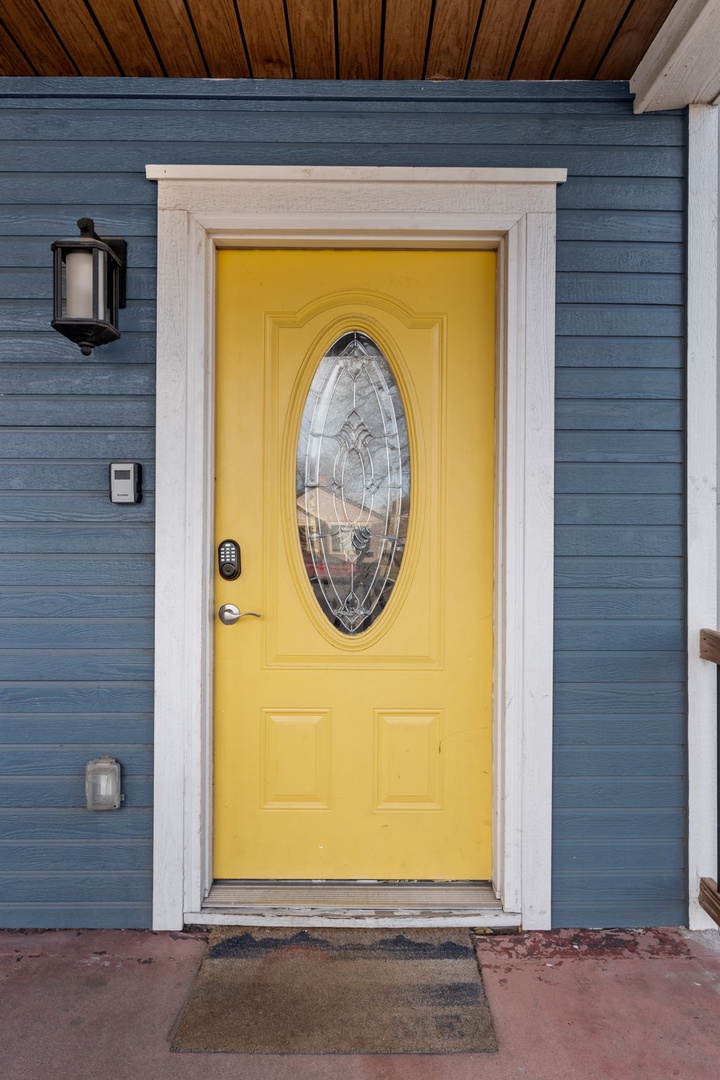 A cheerful yellow door with decorative glass welcomes guests to this charming blue-sided property entrance.