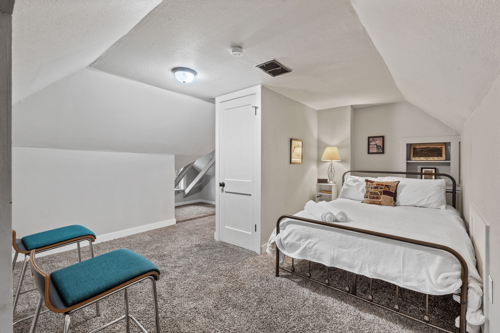 Your cozy attic bedroom features slanted ceilings and thoughtful touches, with crisp linens, soft lighting, and comfortable seating for a peaceful night's rest.