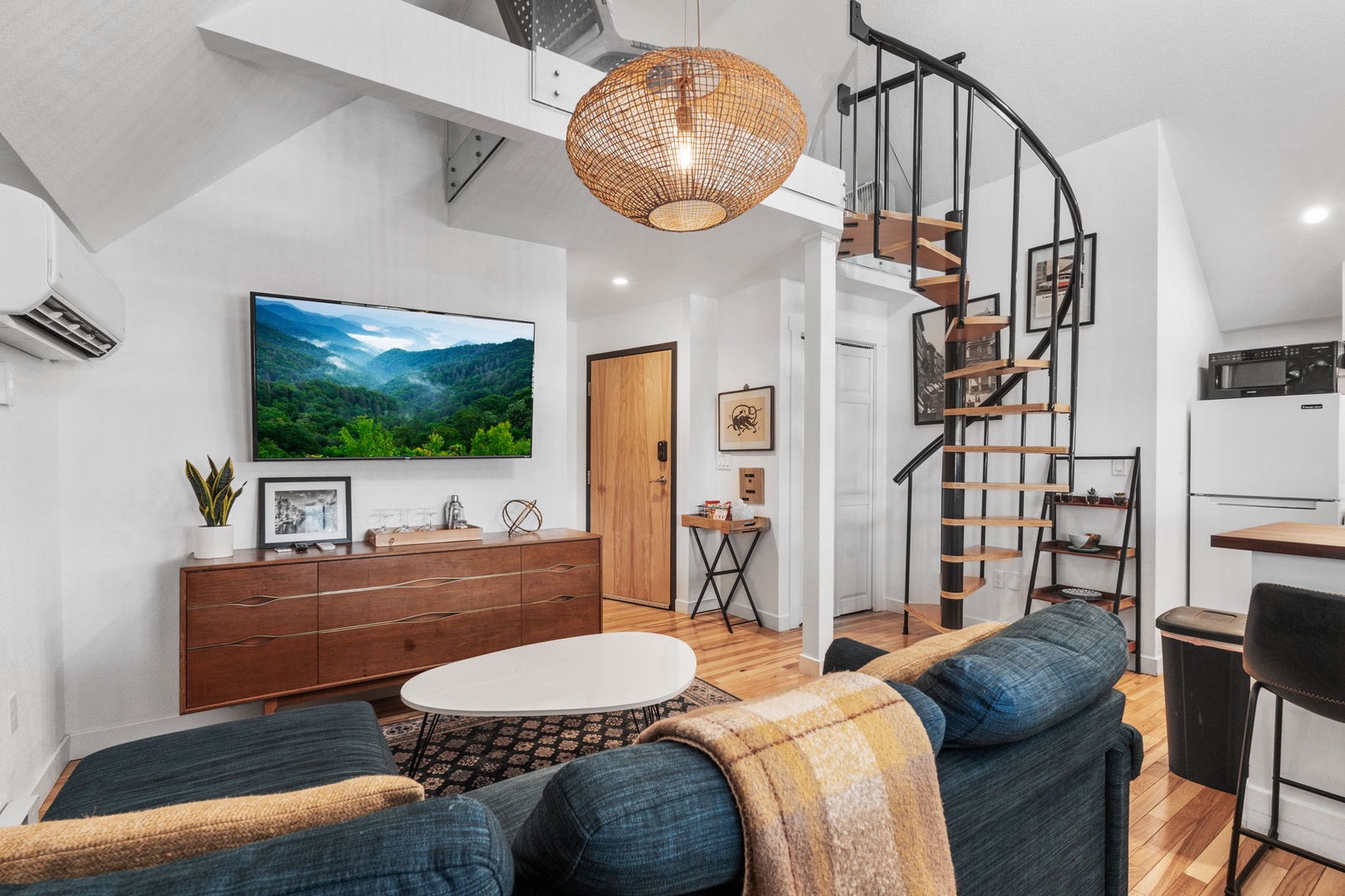 Unwind in your stylish living space with exposed beams, spiral staircase, and cozy seating perfect for movie nights.