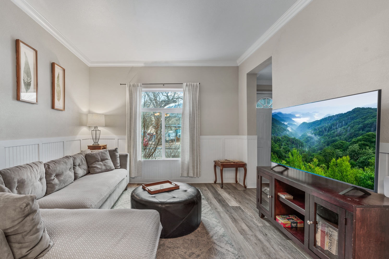 Relax in your elegant living room with plush seating, modern entertainment center, and peaceful neighborhood views through large windows.