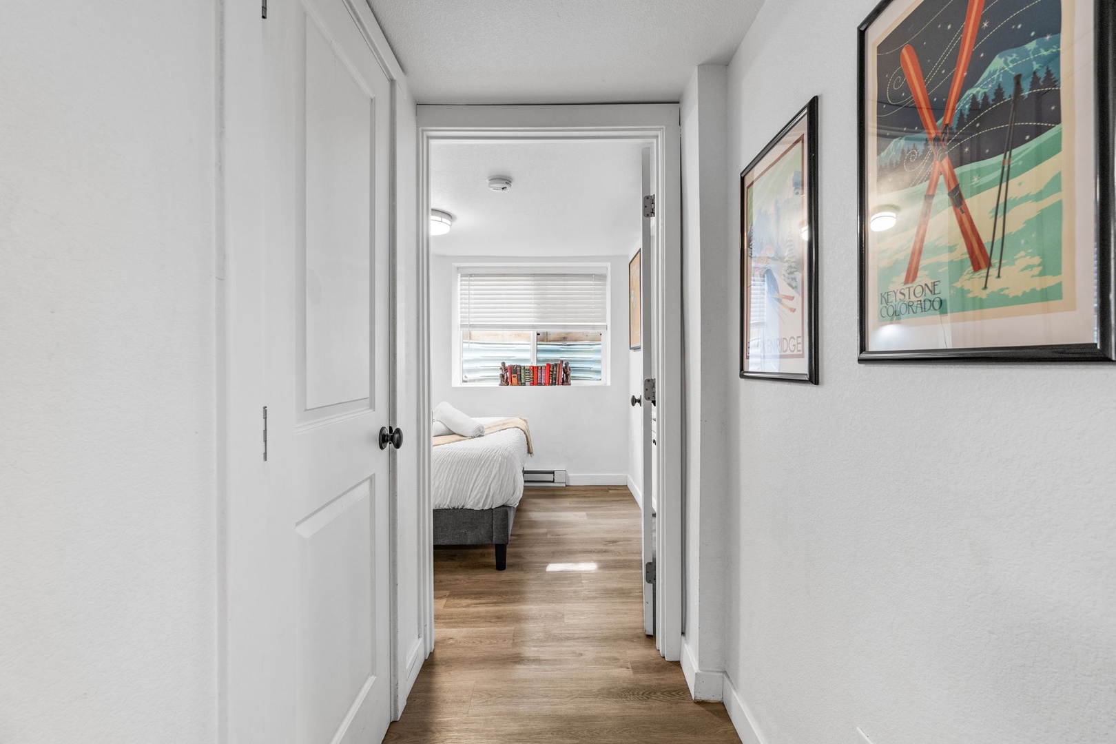 You'll find yourself in a bright hallway adorned with vintage art, leading to your cozy bedroom with warm wood floors.