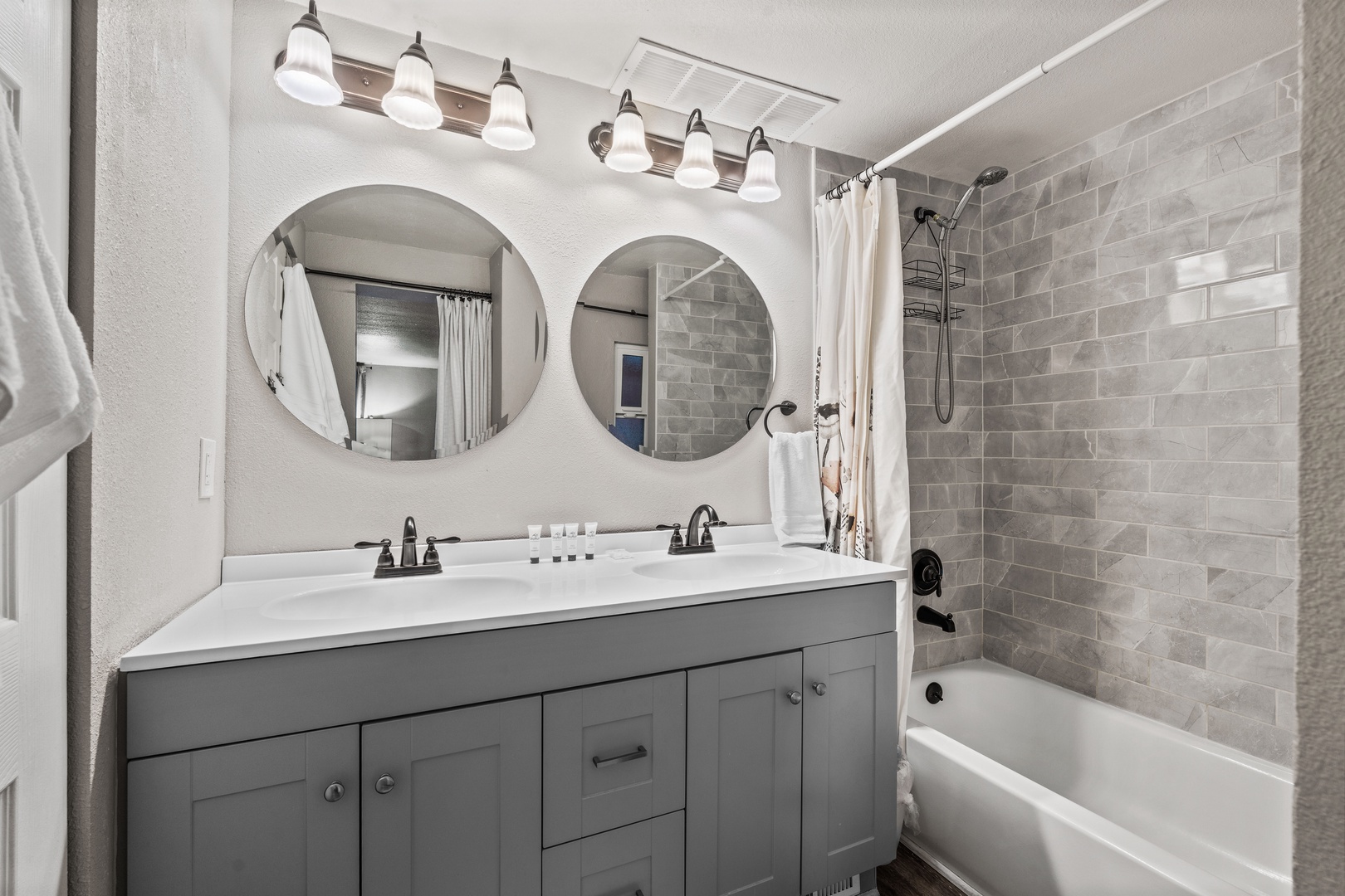 Step into your beautifully designed bathroom featuring dual vanities with elegant round mirrors, stylish tile work, and a relaxing tub-shower combination for your comfort.