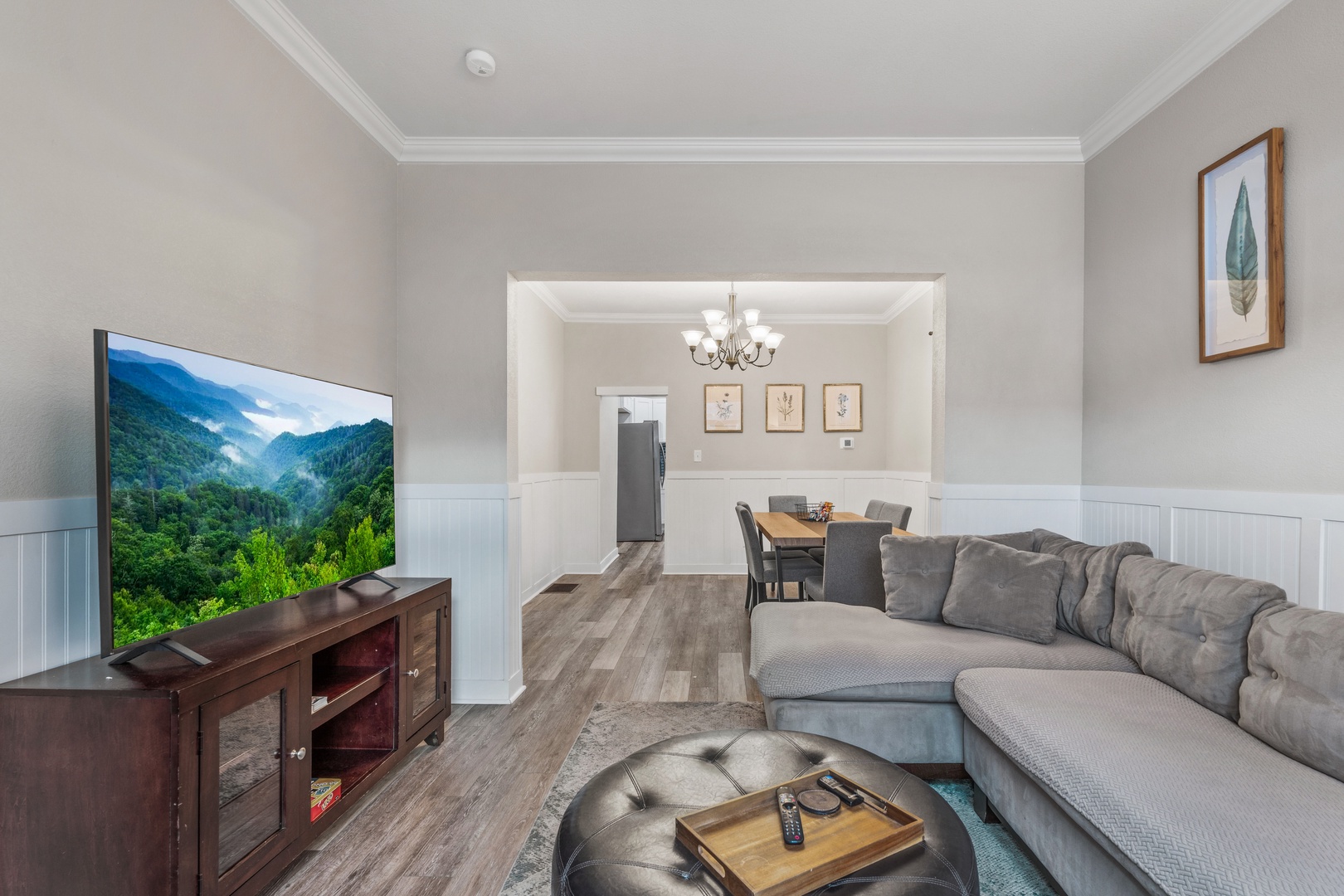 Relax in your spacious living room featuring a plush sectional sofa, large flat-screen TV, and elegant decor that flows seamlessly into the dining area.
