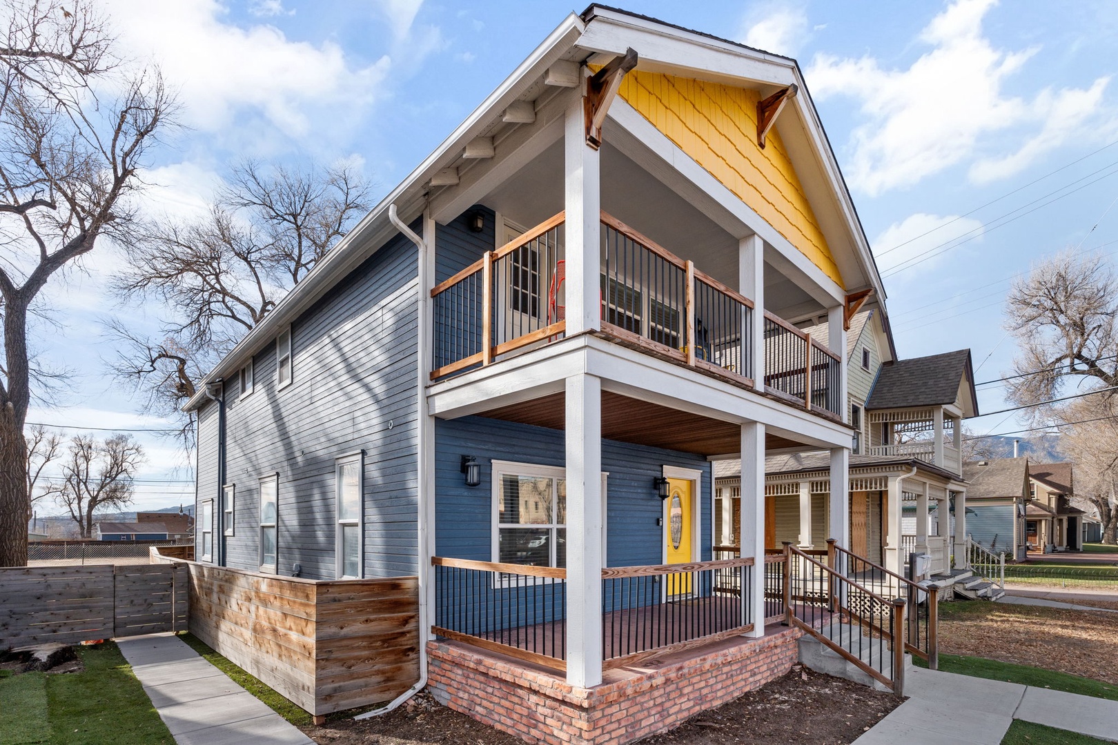 Charming blue cottage with welcoming yellow door and double-story porches in a quiet residential neighborhood.