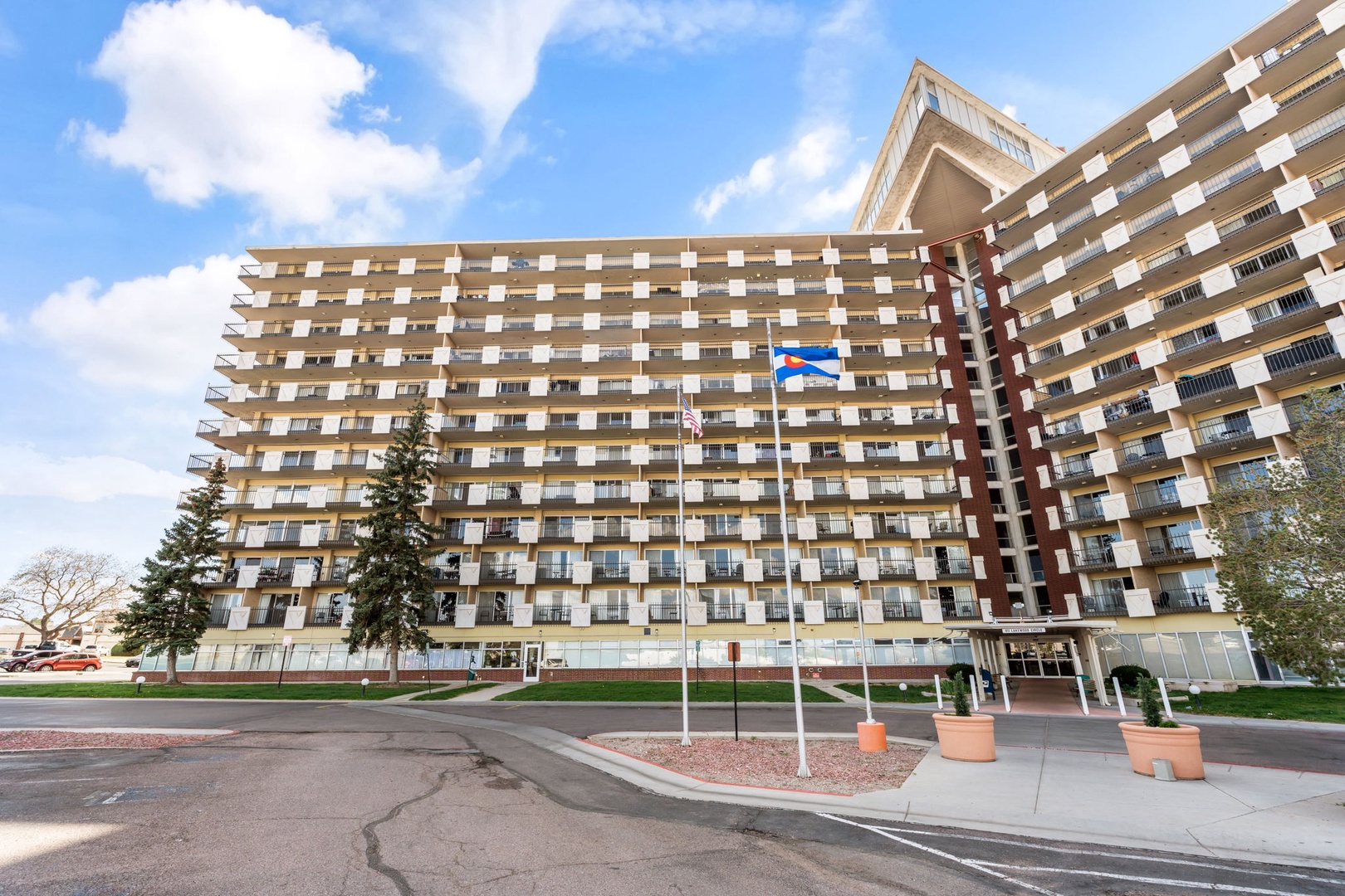 A modern multi-story vacation rental building featuring numerous private balconies, situated in a quiet residential setting with mature trees and open skies.