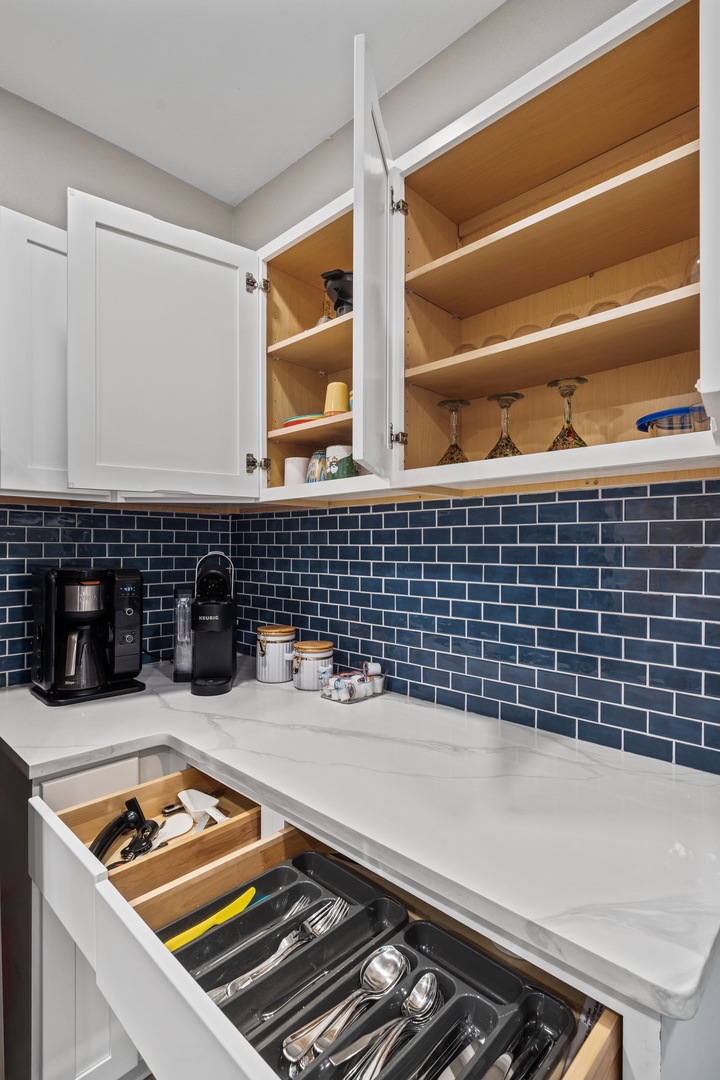Your well-organized kitchen features ample storage with custom pull-out drawers and open shelving, plus a stylish blue subway tile backsplash and convenient coffee station.