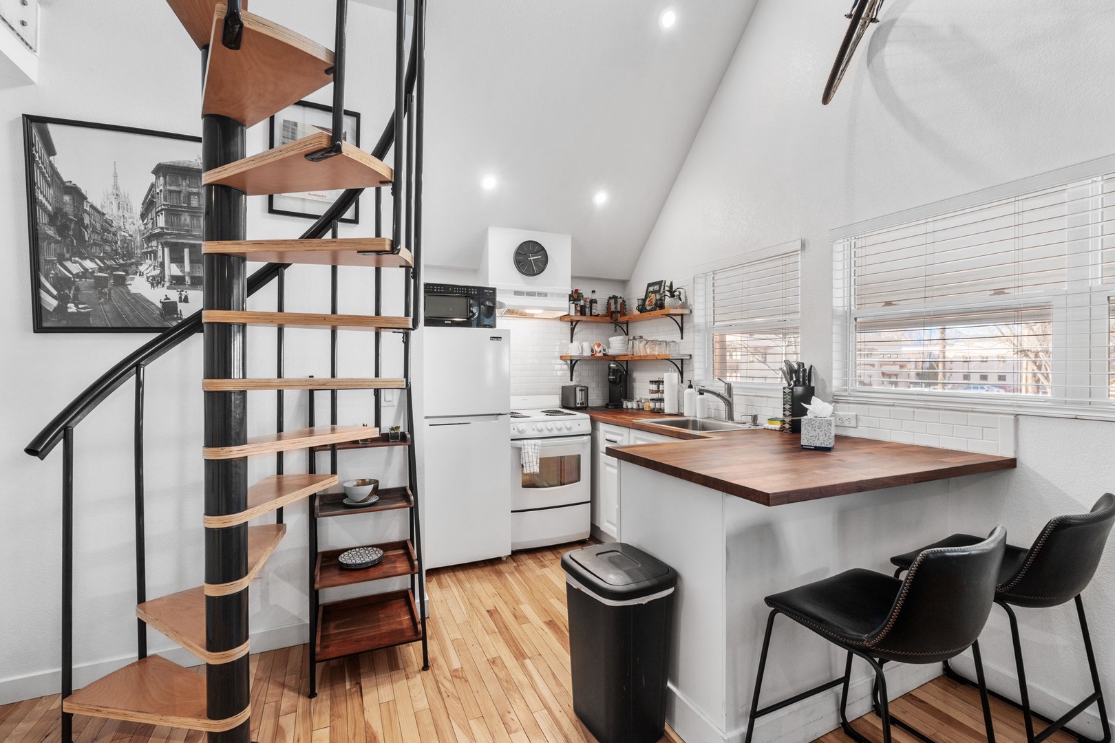 Your modern loft kitchen features sleek white appliances and warm wood countertops, perfect for preparing meals while city views stream through bright windows.