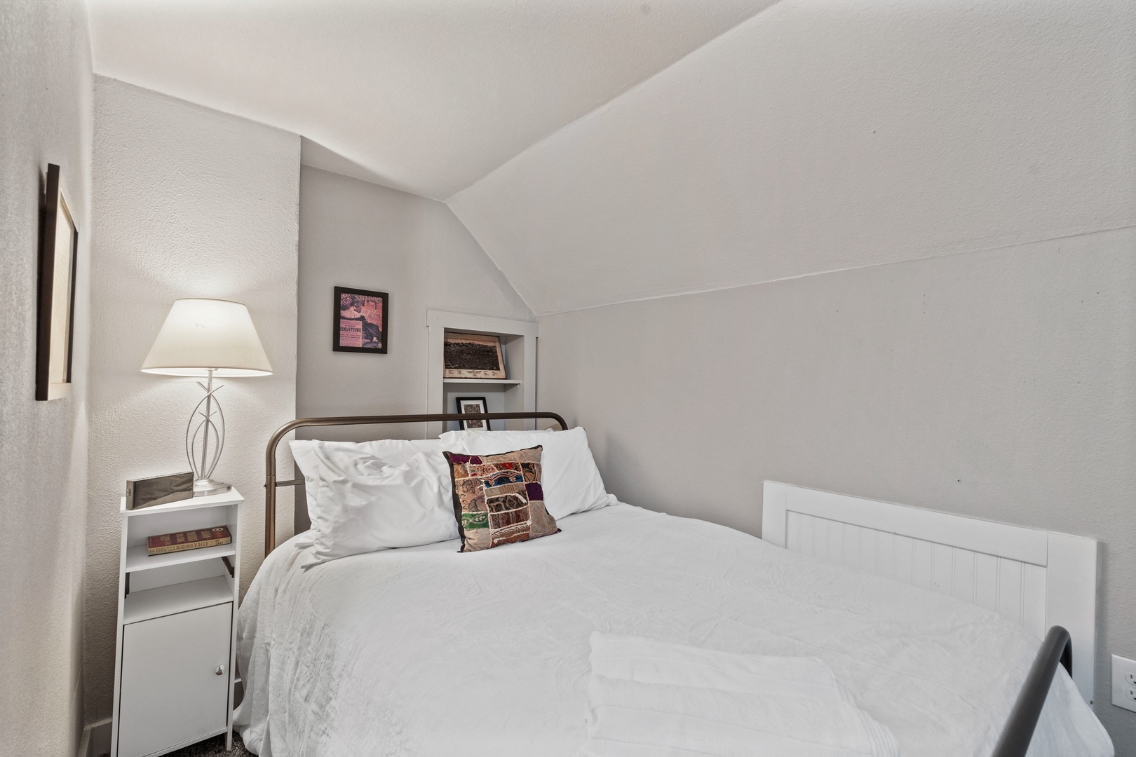 Unwind in your cozy attic bedroom featuring soft linens, warm lighting, and charming sloped ceilings that create an intimate retreat.