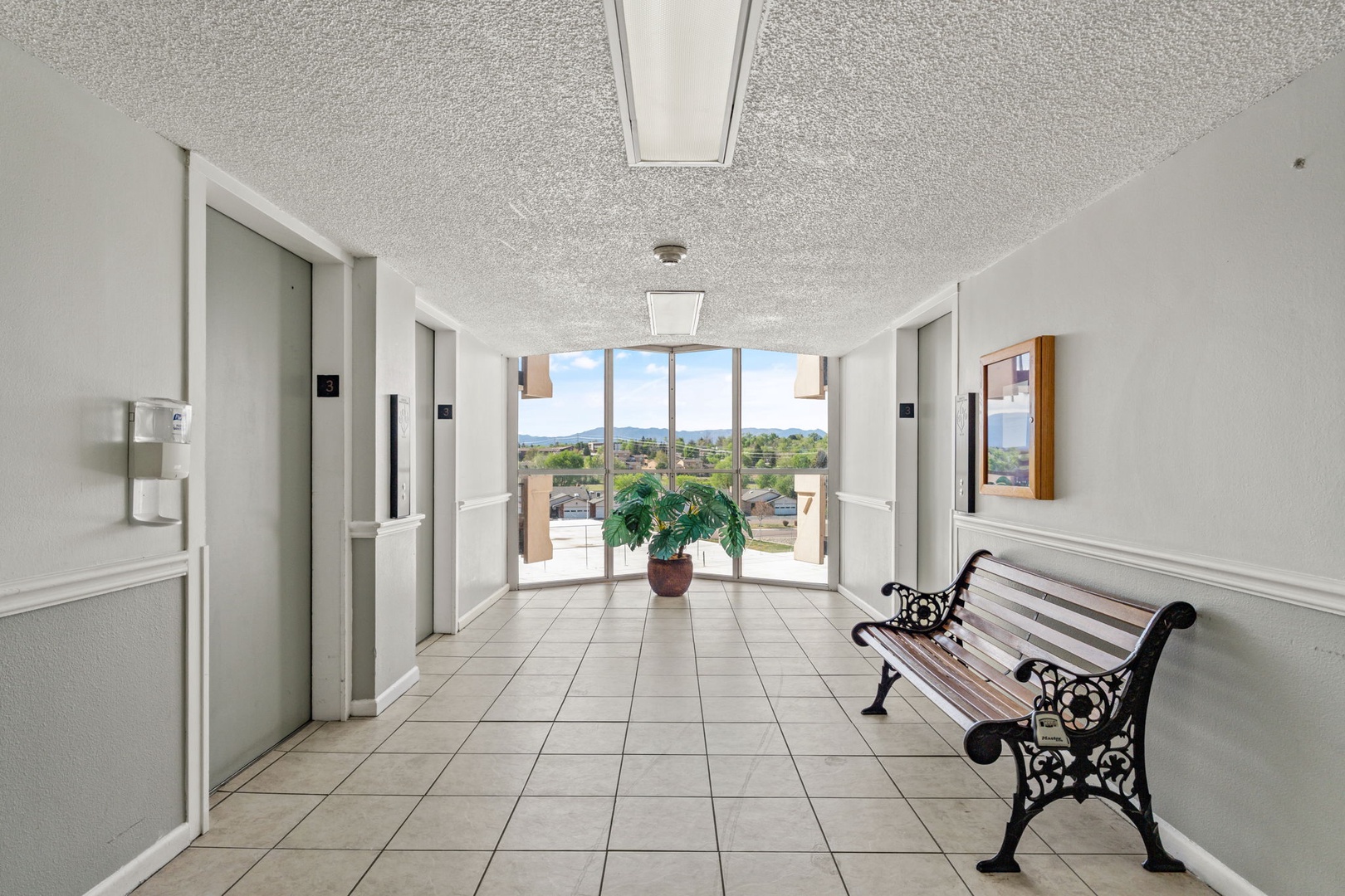 The hallway provides elevator access and welcomes you with a charming bench and plant. Large windows frame scenic city and mountain views as you arrive at your floor.