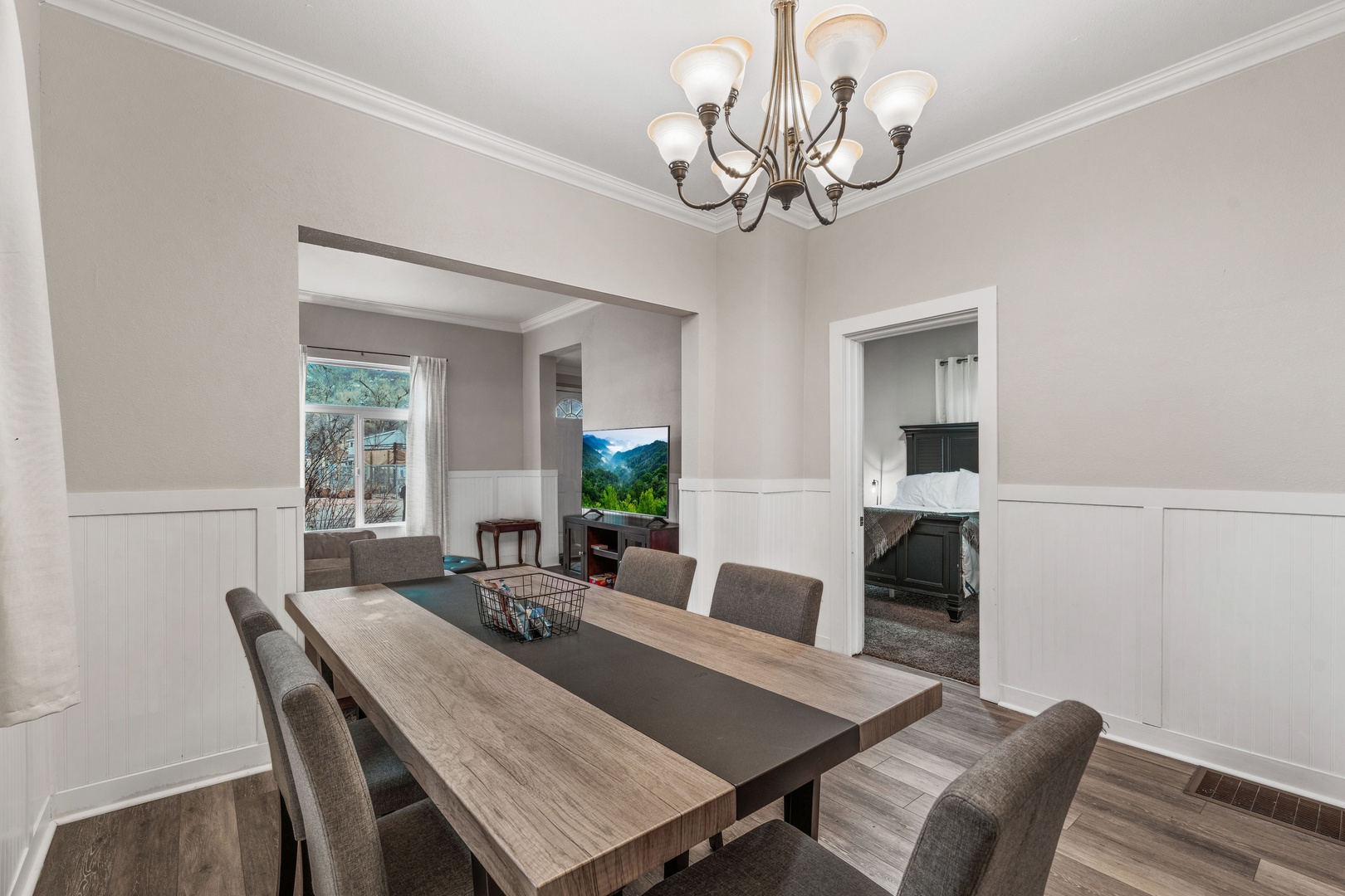 Gather around your elegant dining table beneath a stunning chandelier, with a cozy living area and glimpses of the kitchen just steps away.