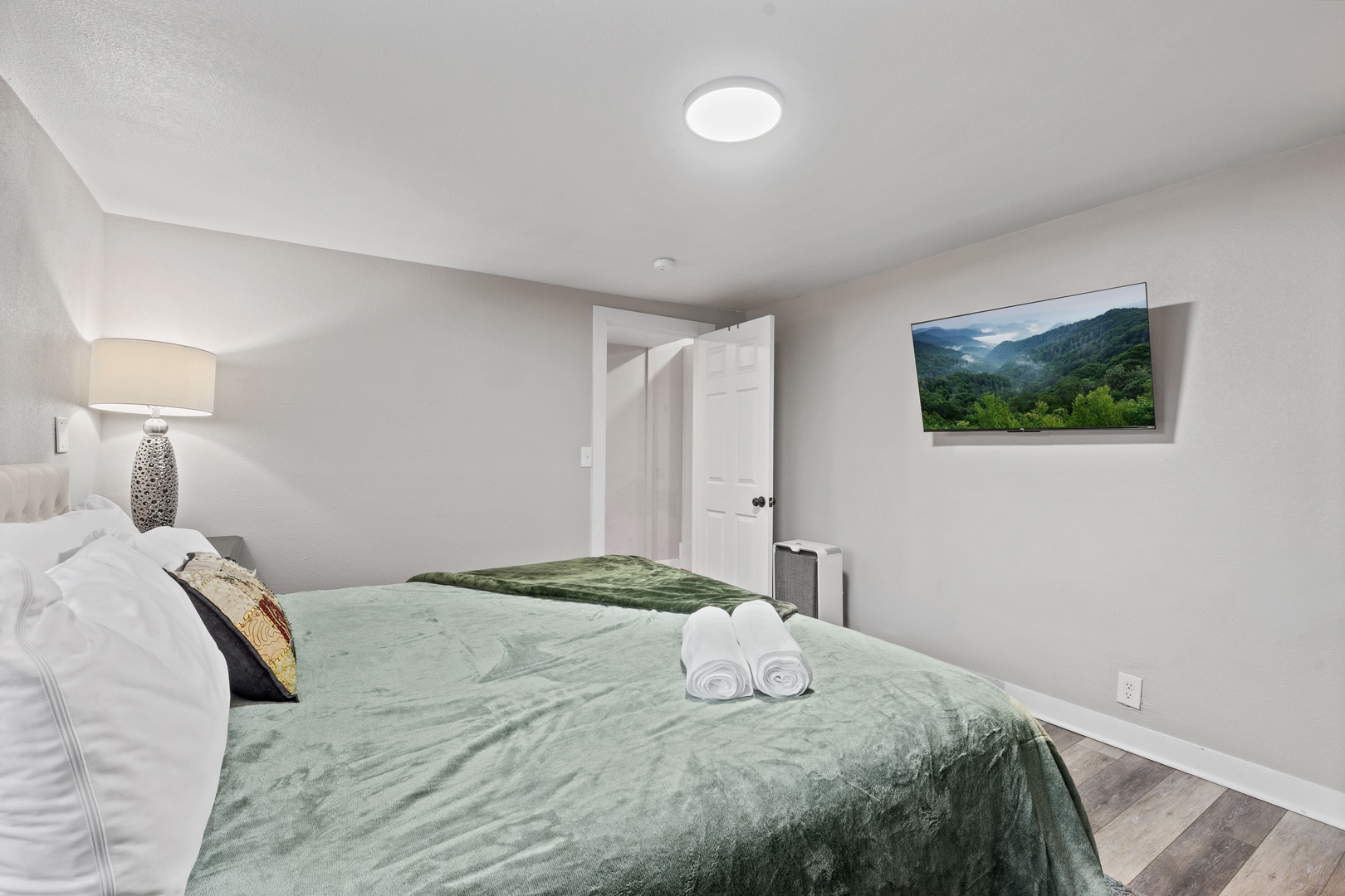 Drift off to peaceful sleep in your cozy bedroom, complete with plush linens, ambient lighting, and thoughtful touches like fresh towels and mountain scenery on the wall-mounted TV.