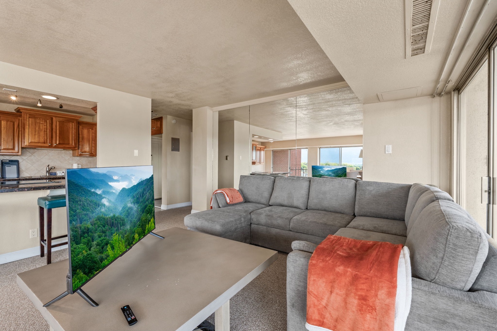 Unwind on the plush sectional as natural light fills your open living space. Your fully equipped kitchen stands ready, while scenic mountain views echo from the large TV—perfect for relaxed evenings in.