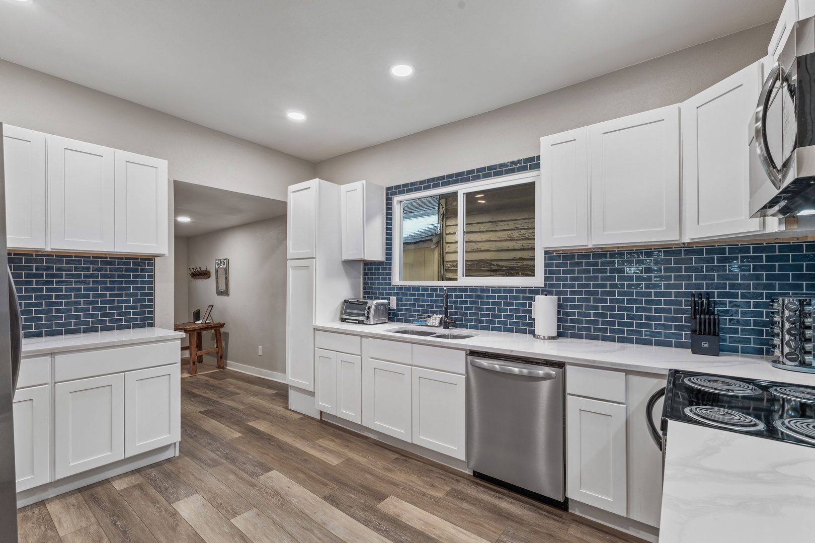 Spacious modern kitchen with crisp white cabinetry, stylish blue subway tile backsplash, and stainless steel appliances - your perfect space for preparing meals and gathering.