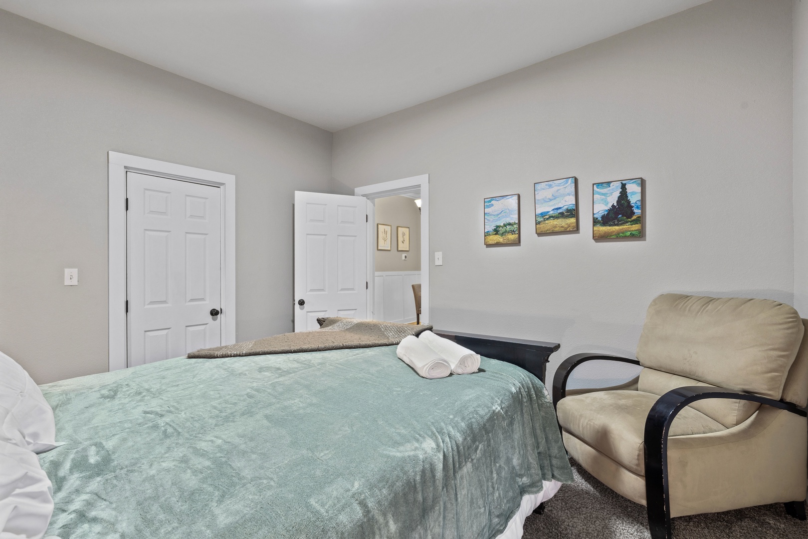 Relax in your comfortable bedroom featuring a cozy bed with fresh linens, peaceful artwork, and a plush reading chair for quiet moments.