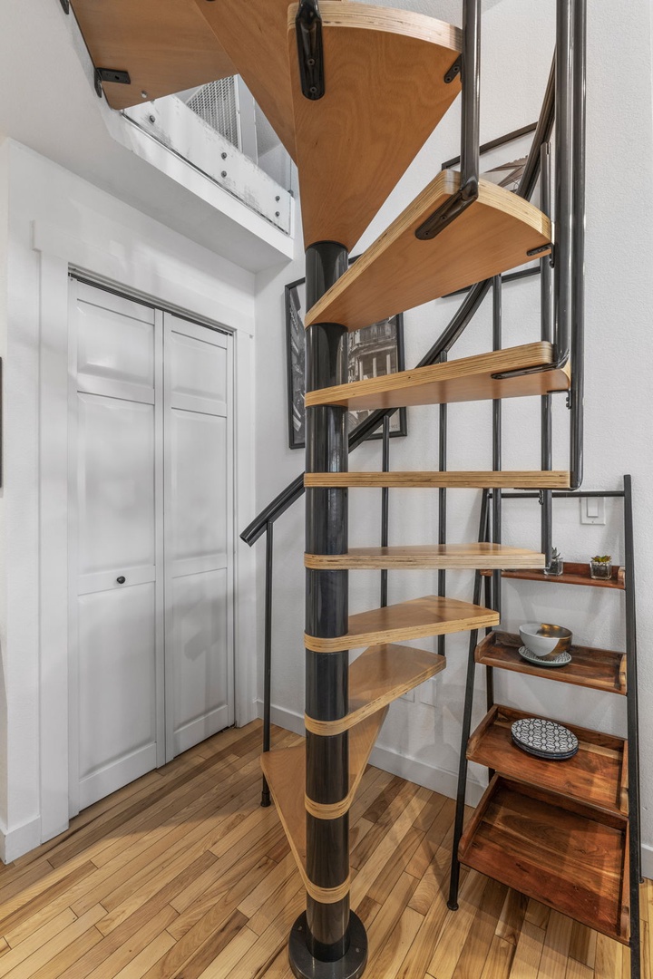 Climb this striking spiral staircase with warm wood steps and sleek metal railings to reach your cozy upper level retreat.