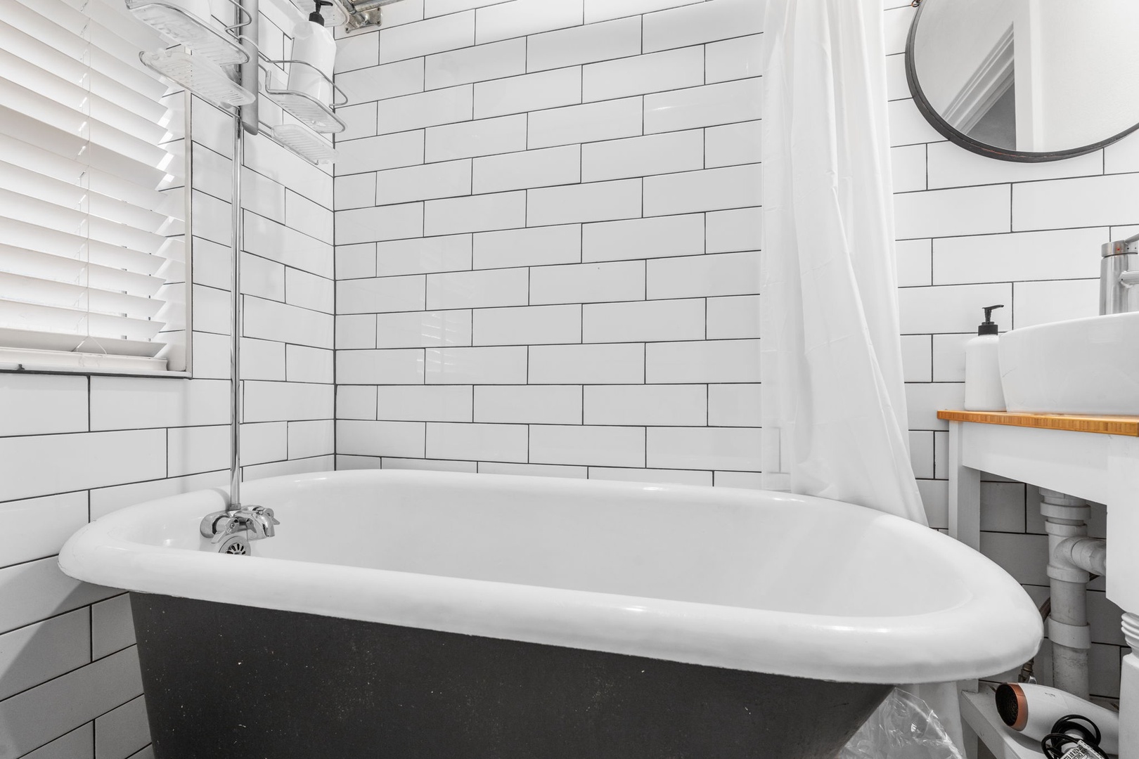 Unwind in your elegant clawfoot tub, surrounded by classic subway tiles and bright natural light from the window blinds.
