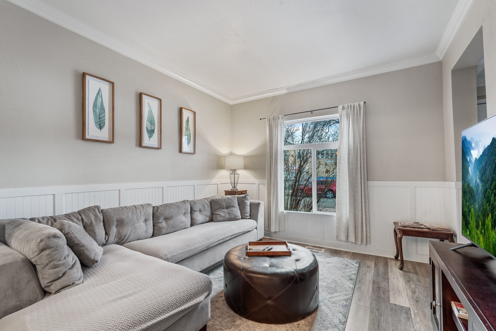 Sink into the plush sectional sofa in your cozy living space, where natural light streams through large windows and thoughtful botanical artwork creates a serene atmosphere.