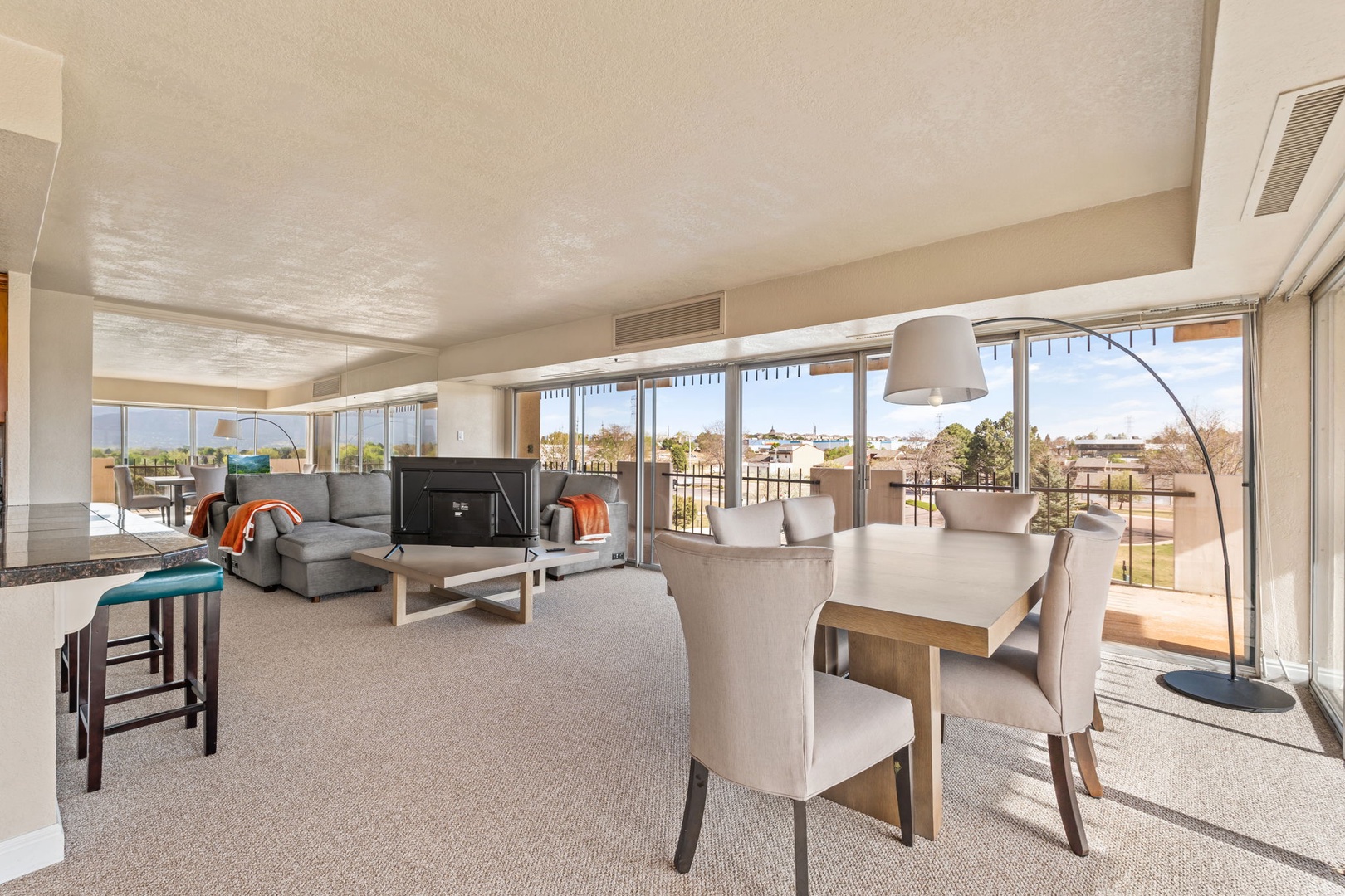 Unwind in your open-concept living and dining area with plush seating, a cozy entertainment setup, and floor-to-ceiling windows framing sunlit views of the surrounding landscape.