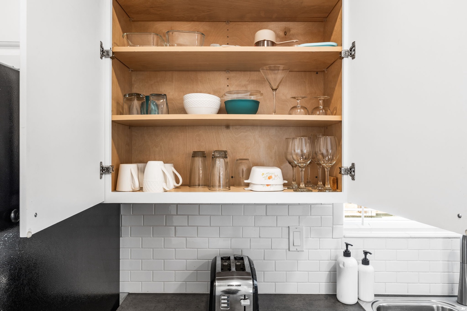 Your well-equipped kitchen cabinet reveals thoughtfully arranged glassware, plates, and essentials for cooking memorable meals during your stay.