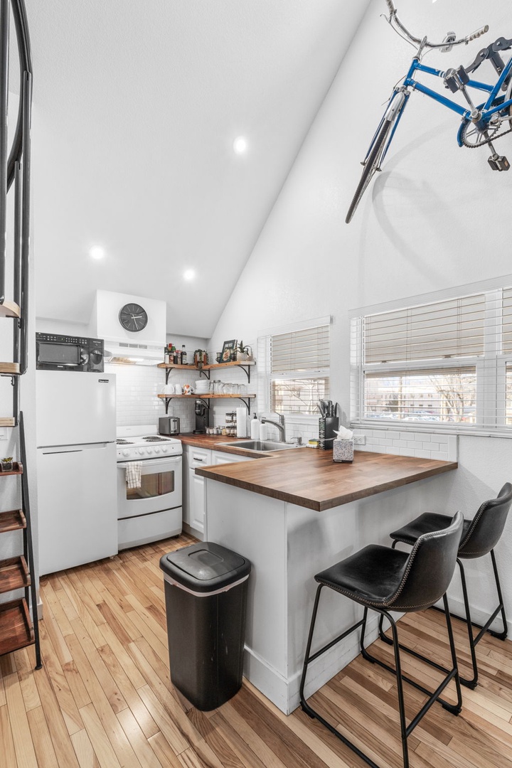 Your modern kitchen features warm wood counters, white appliances, and cozy breakfast seating—perfect for morning coffee or evening meals.